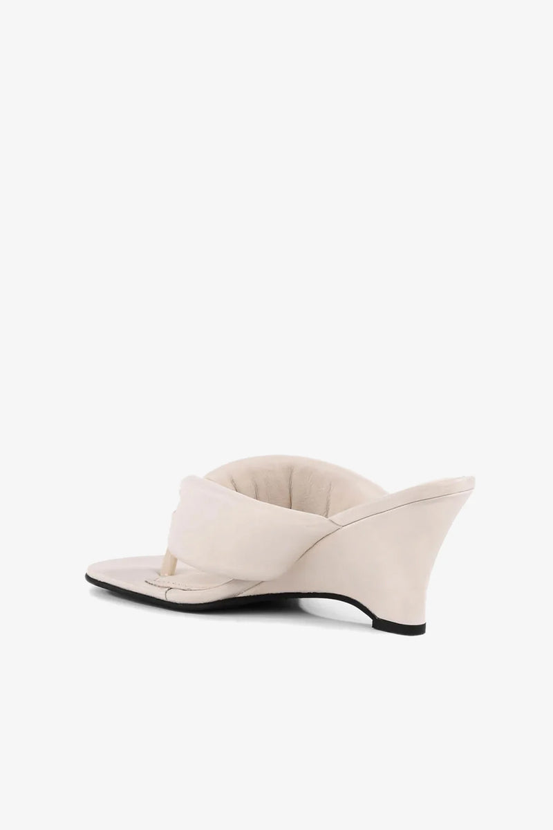 A side view of the Wishing Well Wedge, a beige thong sandal featuring a low wedge heel and cushioned, padded upper, shown on a white background.