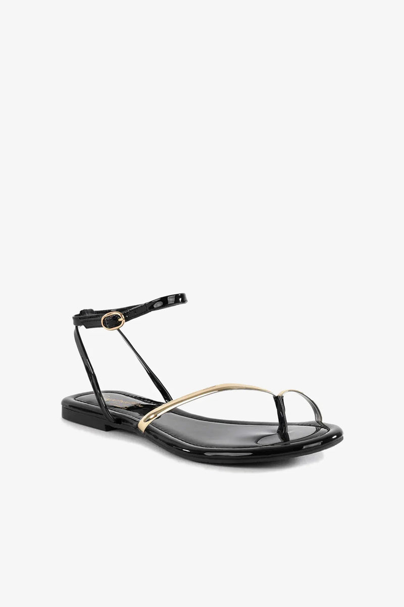 Introducing the A Little Extra Sandal: a black flat sandal featuring a minimalist design with an open toe, thin ankle strap with a gold buckle, and a single gold accent strap across the front. Displayed against a plain white background.