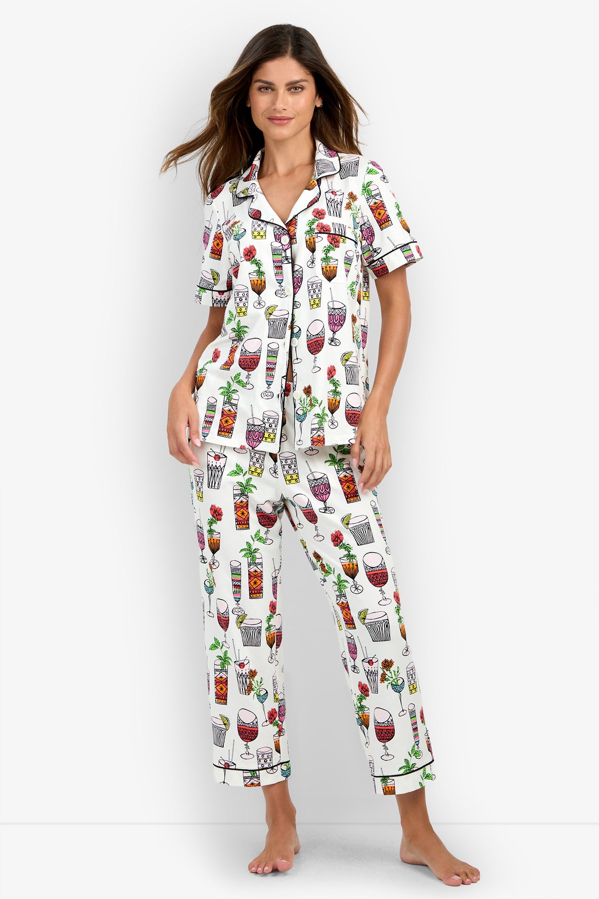 A woman models the Short Sleeve Cropped Pajamas Set, featuring a white fabric with colorful drink and cocktail glass prints, as she stands barefoot against a plain background and looks at the camera.