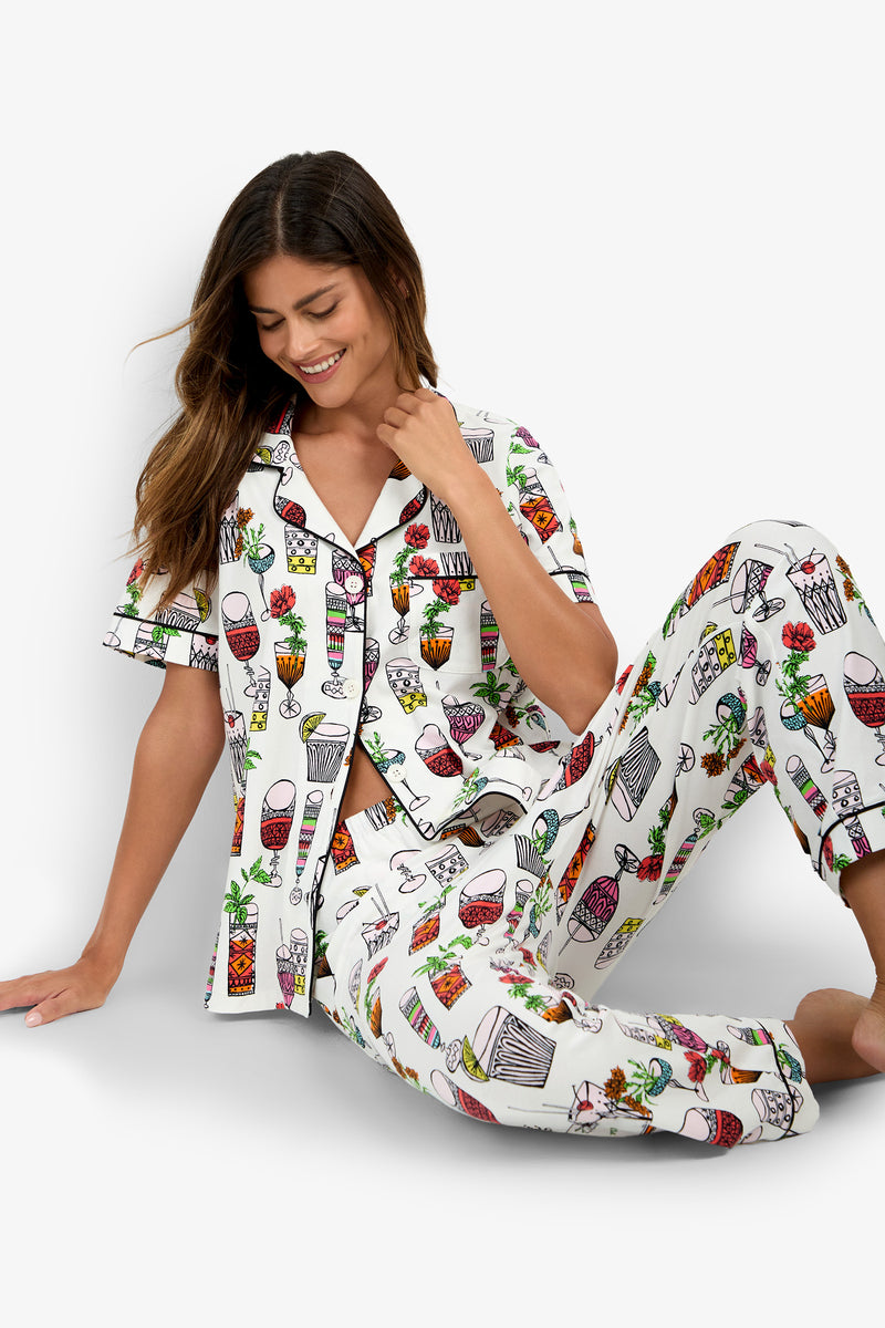 A woman sits on the floor, smiling, wearing the Short Sleeve Cropped Pajamas Set featuring colorful, playful plant and pot designs.