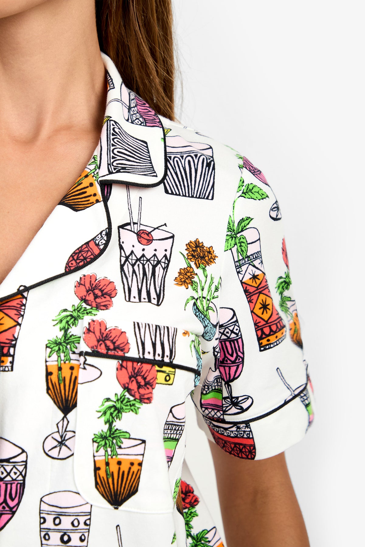 Close-up of a person’s upper body wearing the Short Sleeve Cropped Pajamas Set, featuring a white shirt adorned with colorful cocktail glass and flower illustrations. Only part of the face and neck are visible, set against a plain white background.