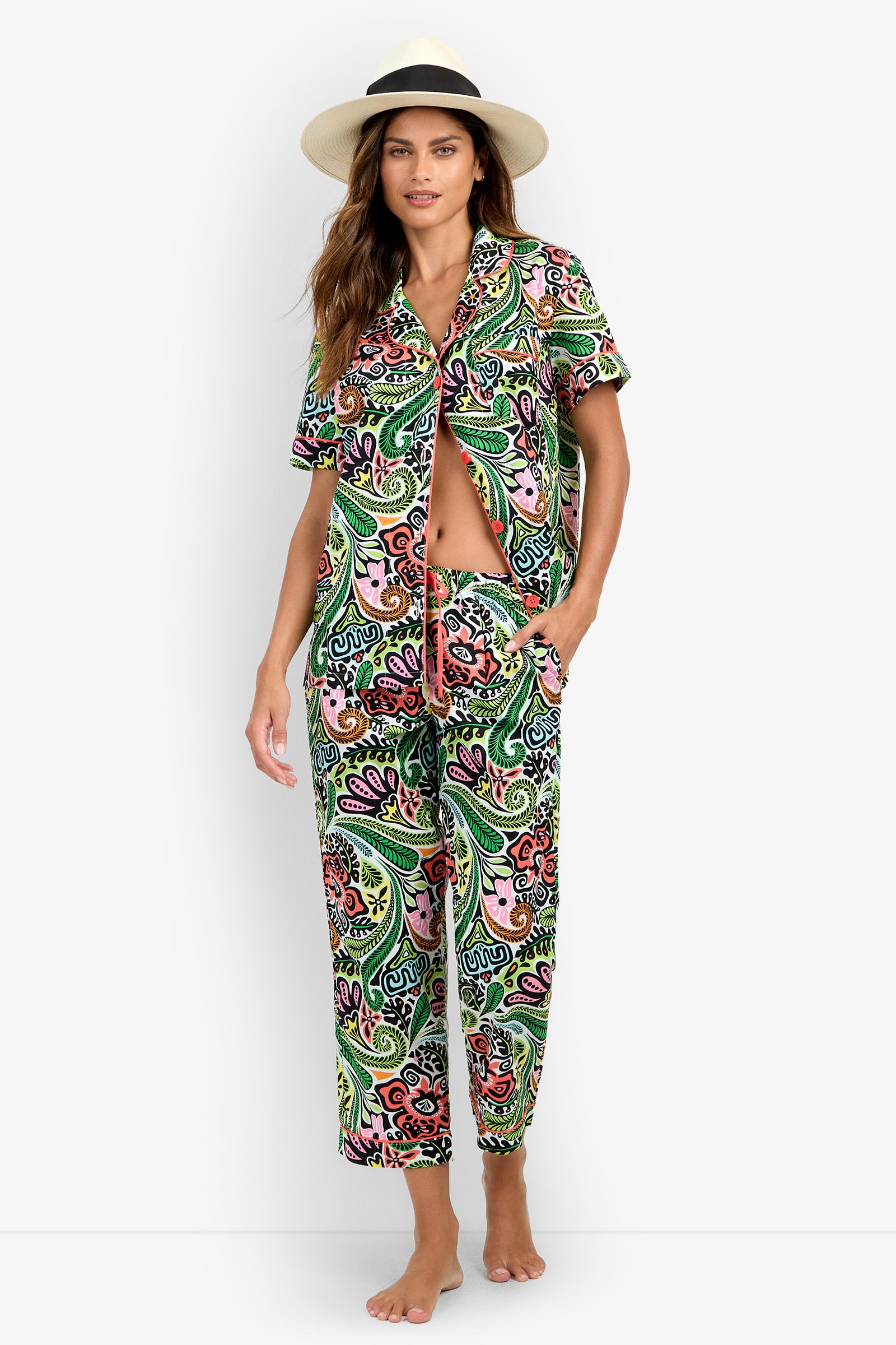 A woman wearing the Short Sleeve Cropped Pajamas Set—a colorful, paisley-patterned matching shirt and pants ensemble—with a beige hat, stands barefoot against a white background.
