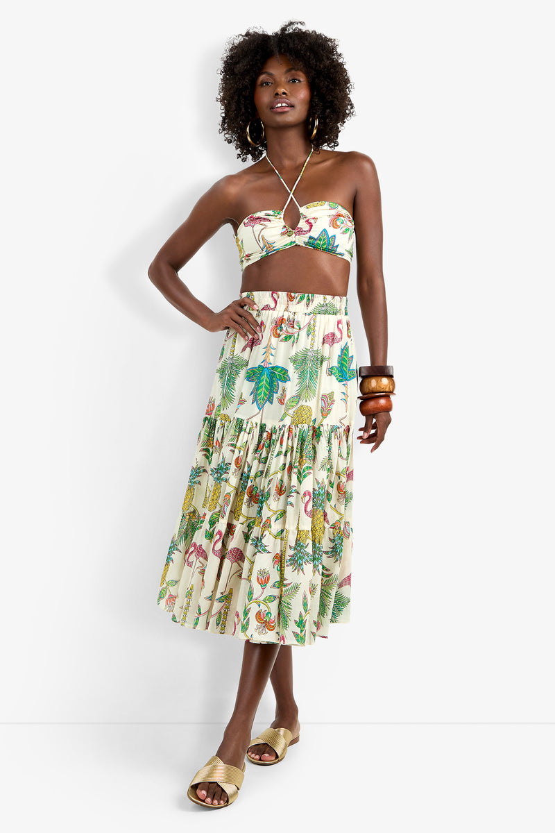 Woman wearing the Marisalle Top, a strapless tropical-print crop top with matching tiered midi skirt featuring colorful leaves, birds, and flamingos; styled with large bangles, hoop earrings, and beige slide sandals.