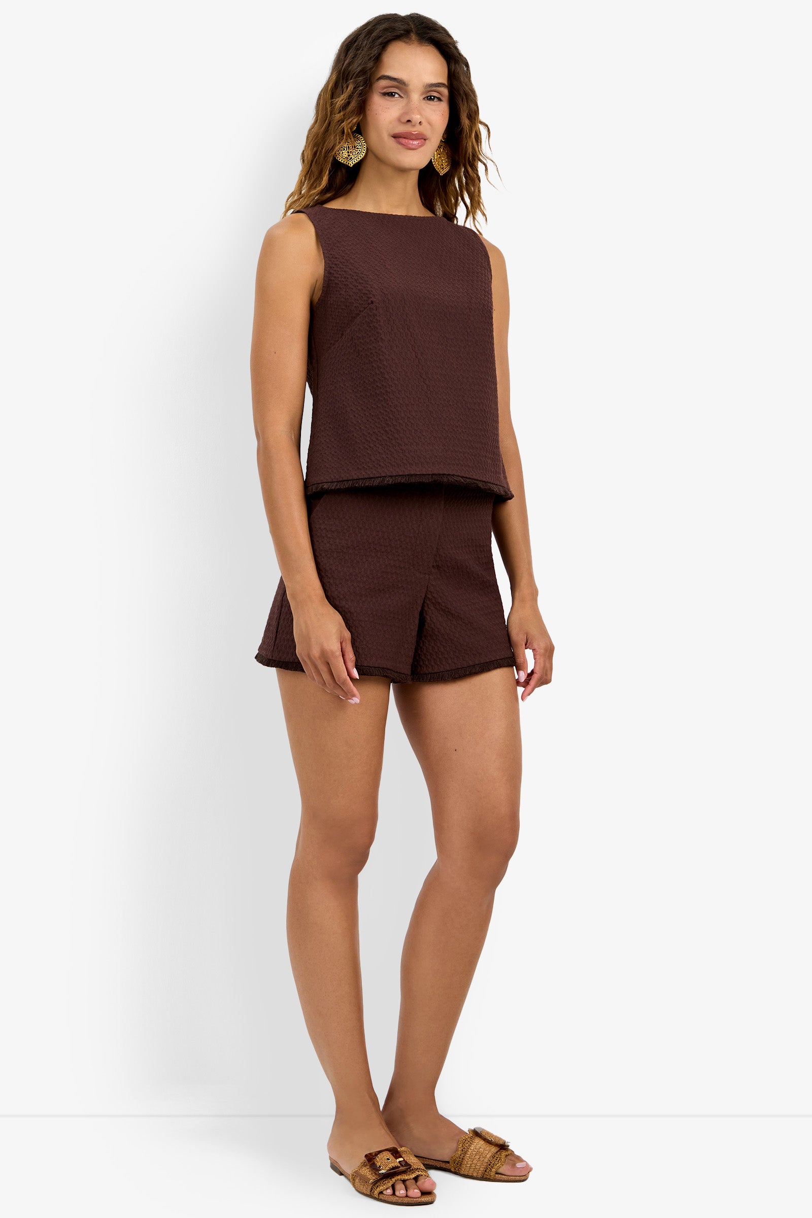 A woman with wavy hair wears the Port Top, a sleeveless dark brown textured top, paired with matching shorts and brown slide sandals against a plain white background.