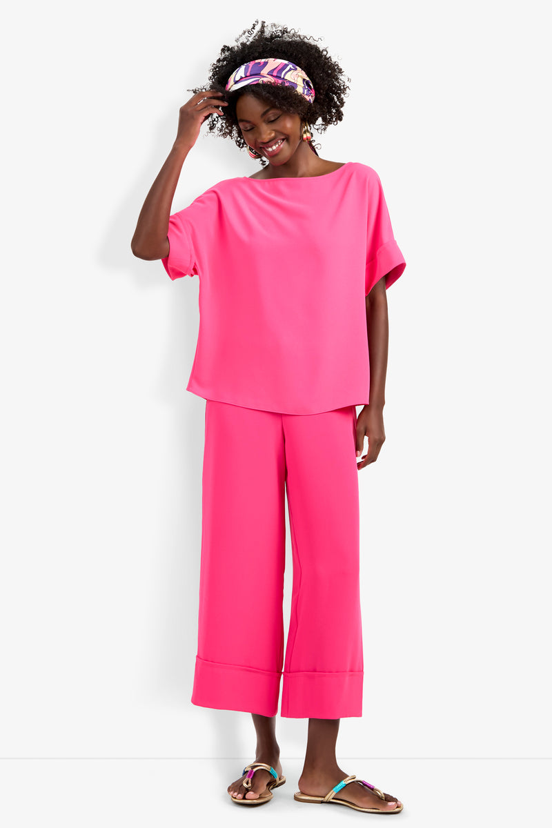 A woman with curly hair in a colorful headband smiles, wearing the Bahooka Pant and a loose, bright pink short-sleeve top, paired with sandals.