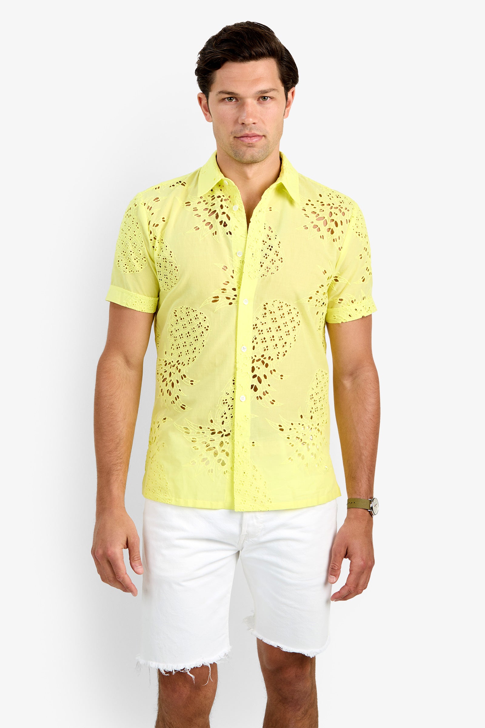A man wearing the BRANSON SHIRT, a light yellow, short-sleeve 100% cotton button-up with eyelet details, and white frayed hem shorts stands against a plain white background.