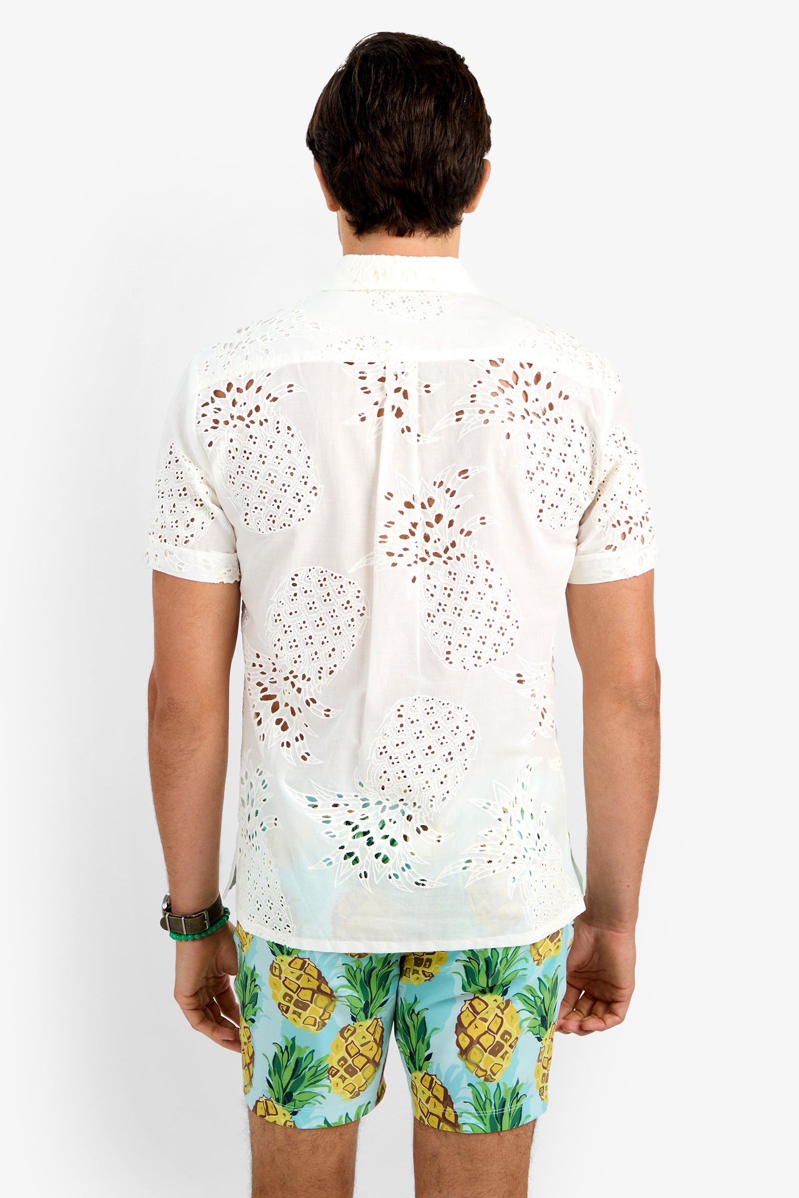 A man stands with his back to the camera, wearing a white short-sleeve BRANSON SHIRT and colorful pineapple-print shorts against a plain white background.
