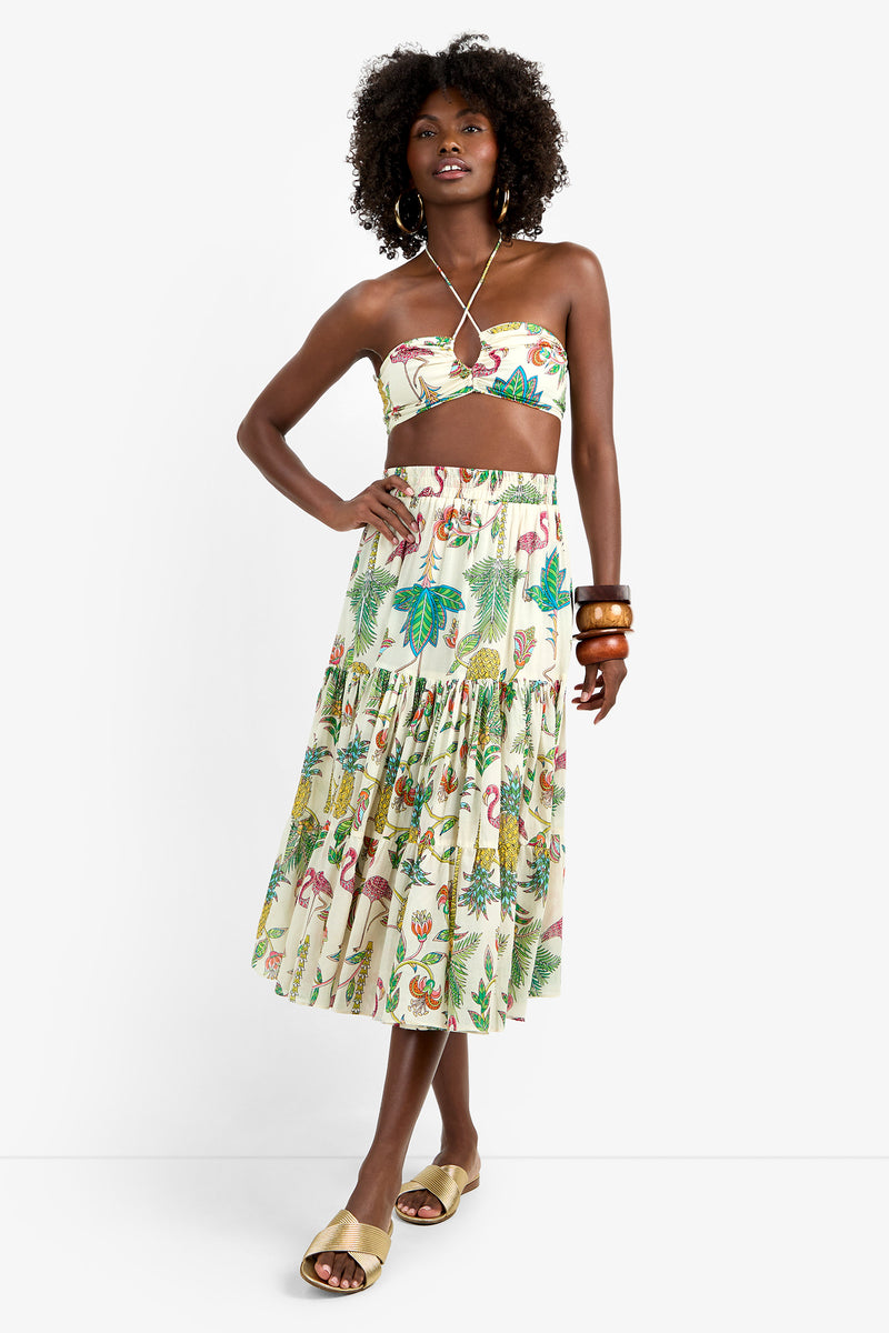 Woman in MARSAY SKIRT, a 100% cotton tiered midi with colorful tropical print, paired with strapless crop top, tan slide sandals, wooden bangles, and hoop earrings against a white background.