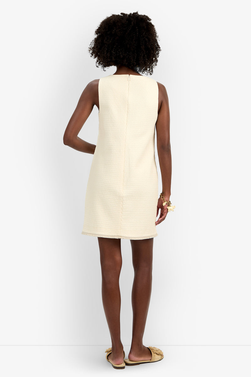 A woman with curly hair stands facing away, wearing the sleeveless, textured cream Waveson Dress and beige slide sandals against a white background.
