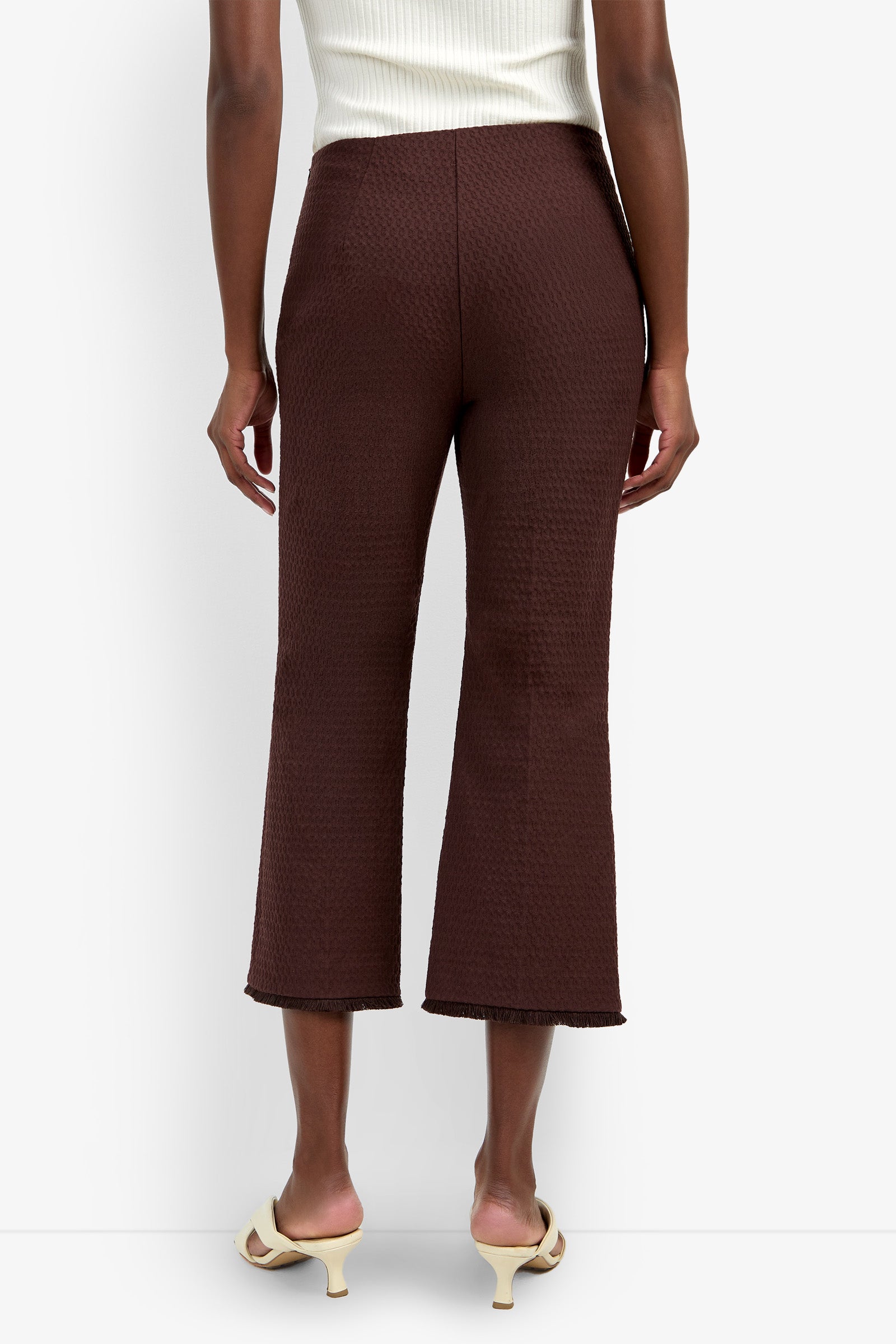 A person wearing the Gulf Pant in a textured brown fabric and cream heeled sandals, standing with their back to the camera. The person is also wearing a sleeveless white top.