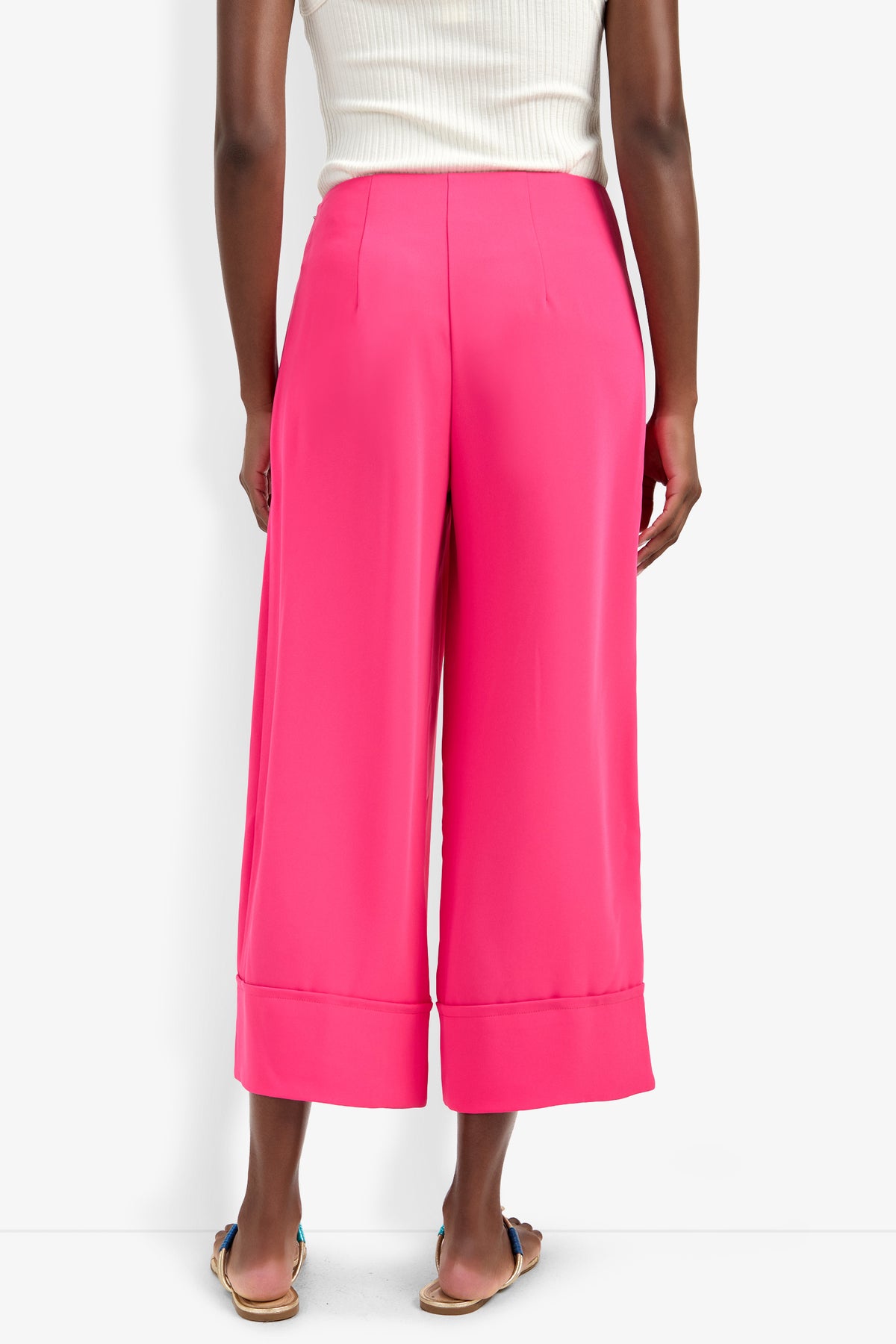 A person is seen from the back wearing the Bahooka Pant in bright pink, styled with a white sleeveless top and flat sandals, all set against a white background.