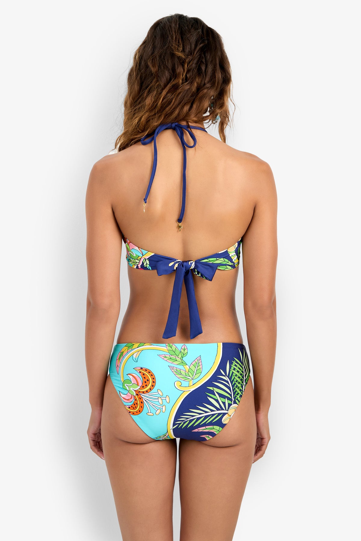A woman is shown from the back wearing a Bandeau Bikini Top with a blue tie and a vibrant tropical pattern in blue, green, and orange.