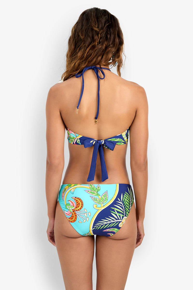 A woman is shown from the back wearing a Bandeau Bikini Top with a blue tie and a vibrant tropical pattern in blue, green, and orange.