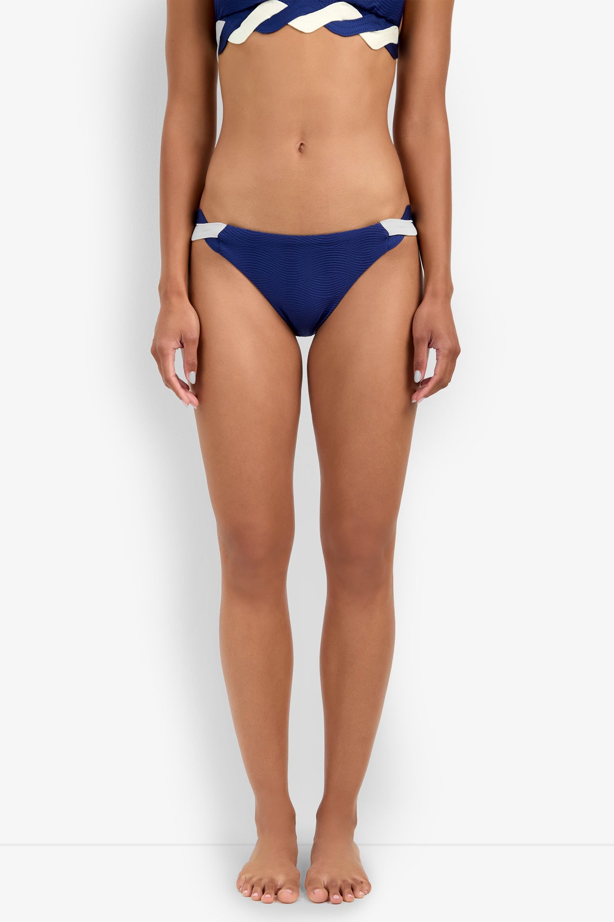 A woman stands barefoot against a plain white background, wearing the Hipster Bikini Bottom in blue with white accents and a matching blue and white bikini top.