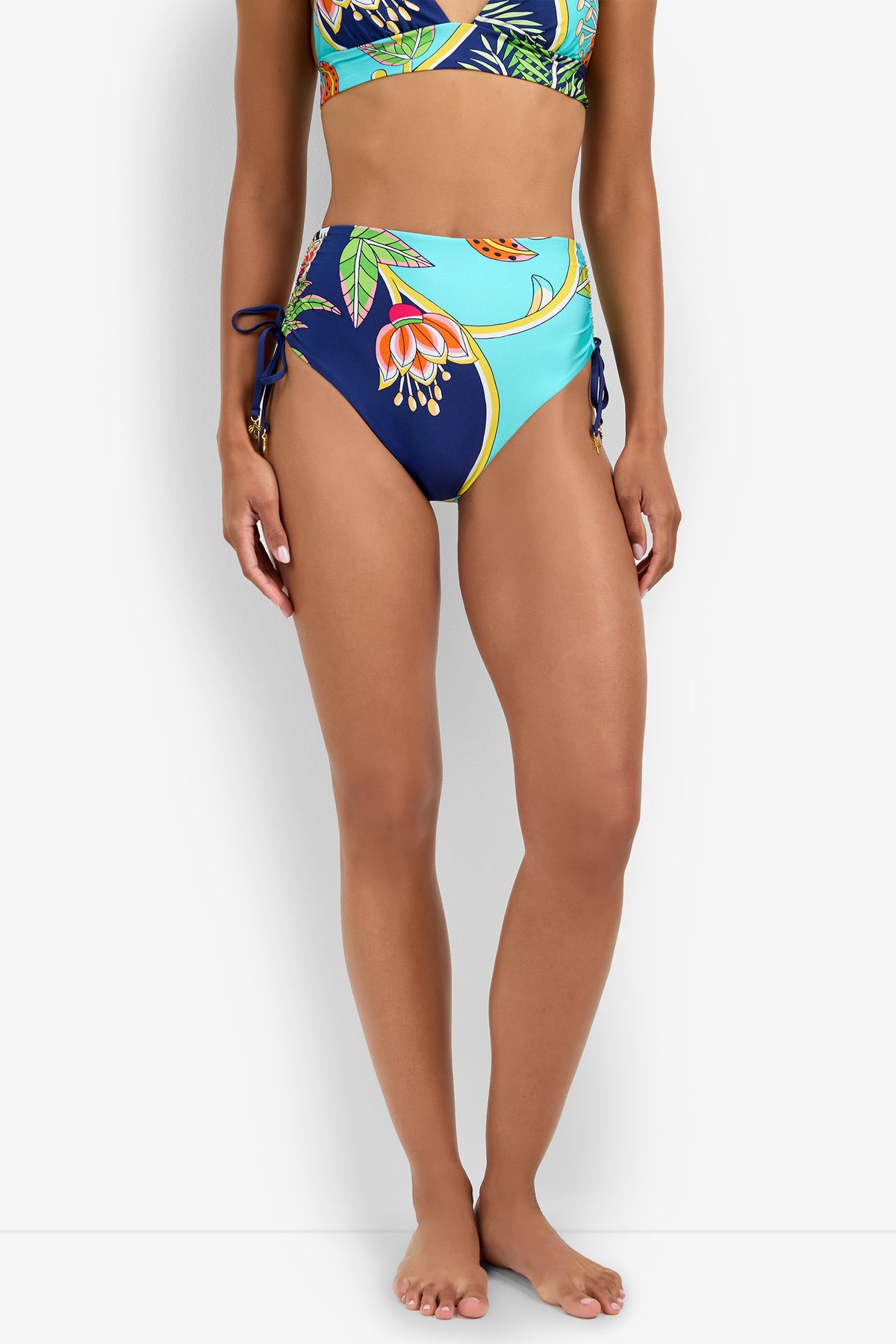 A woman in a High Waist Bikini Bottom with floral print and side ties, paired with a matching top, stands barefoot against a white background.