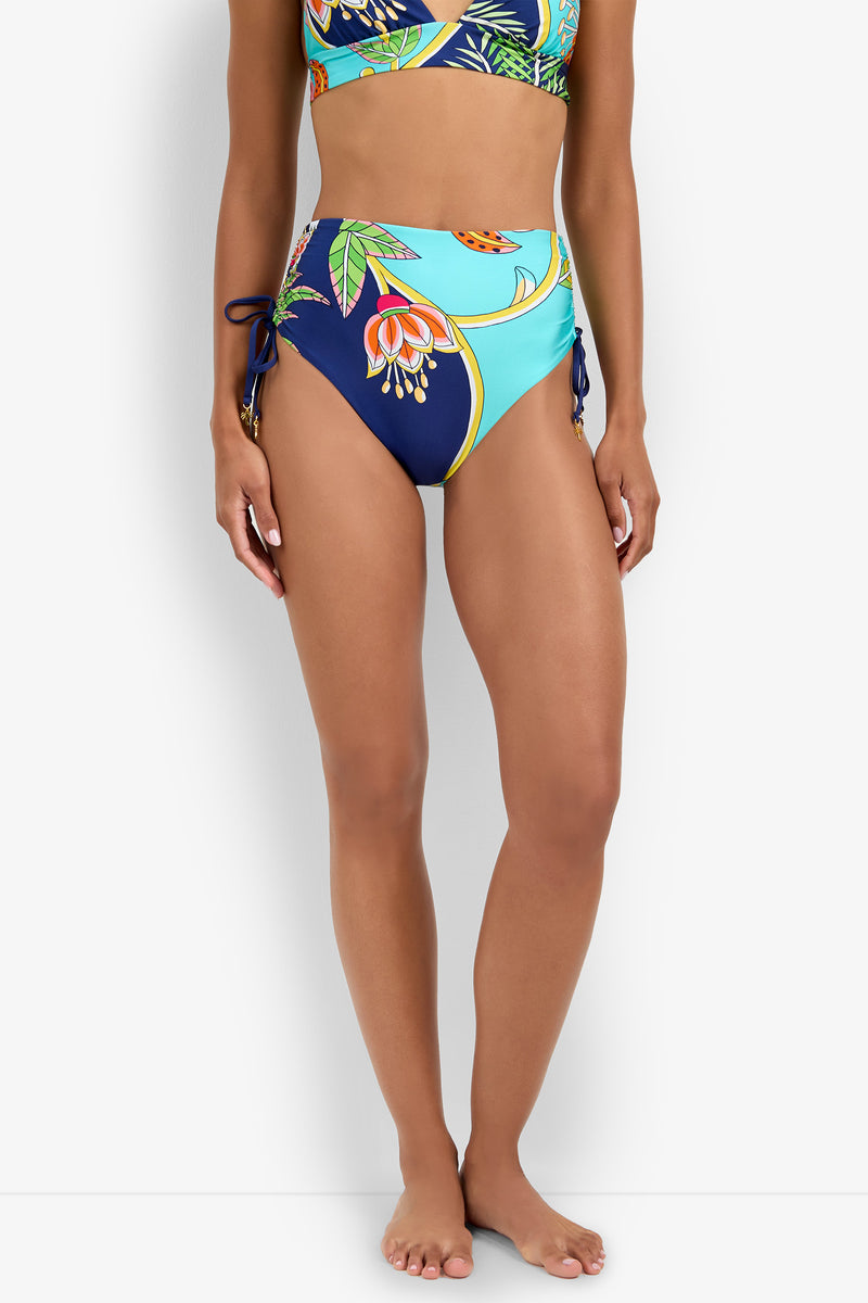 A woman in a High Waist Bikini Bottom with floral print and side ties, paired with a matching top, stands barefoot against a white background.