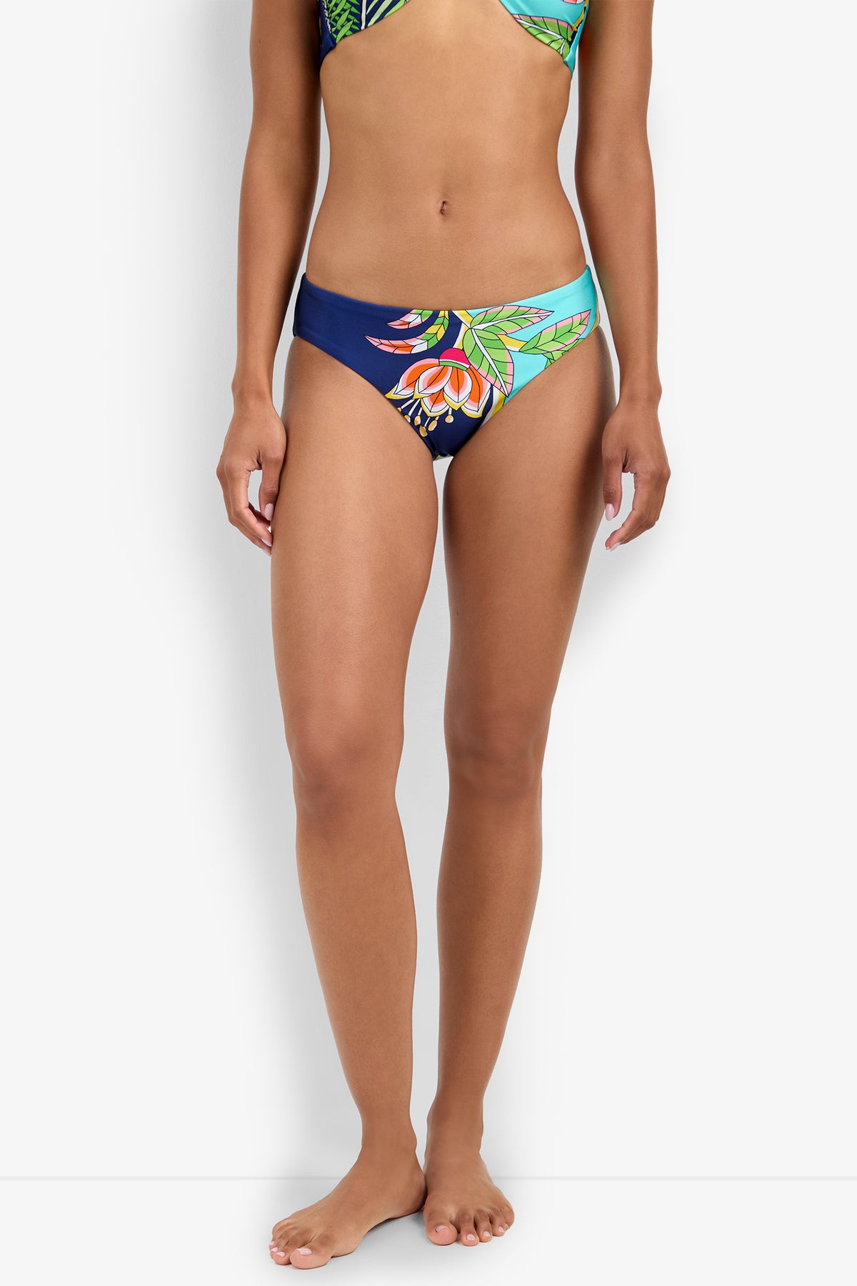 A woman models the Hipster Bikini Bottom featuring a vibrant blue, green, and orange floral print, standing barefoot against a plain white background.