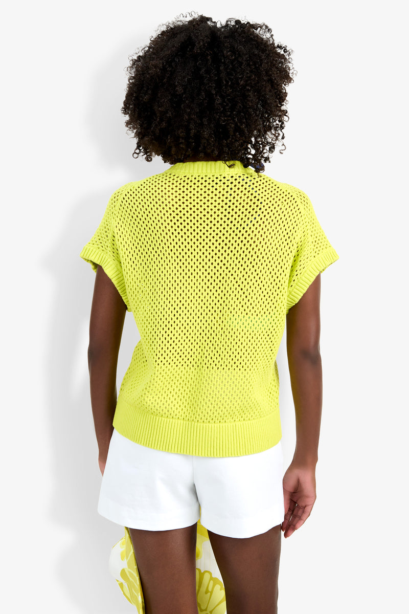 A person with curly hair is seen from behind, wearing the Hana Zip Cardigan—a short-sleeve, bright yellow knit top—paired with white shorts against a plain white background.