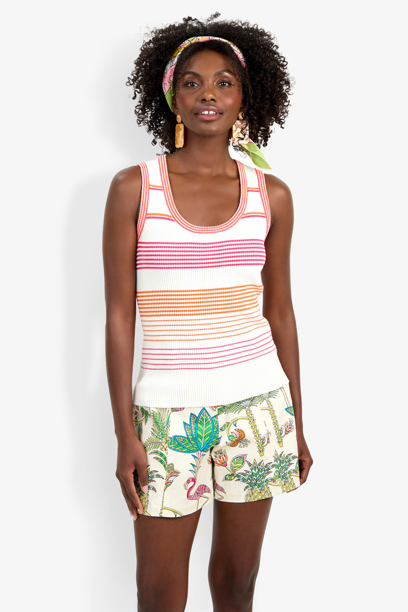 A woman with curly hair, a headband, and statement earrings smiles slightly while wearing the Paolini Tank and tropical-patterned shorts, standing facing forward.