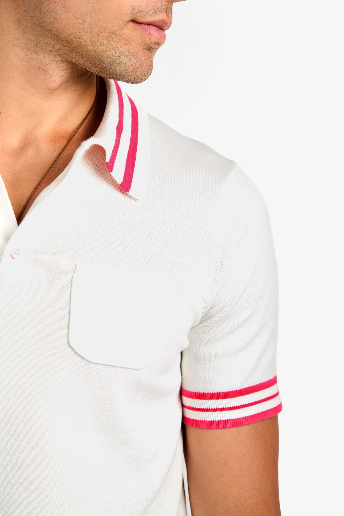 A person wears the JAIME FLAMINGO POLO, a white cotton short-sleeve polo with pink and red striped collar and sleeve cuffs, plus a chest pocket, shown from shoulders to mid-torso against a white background.