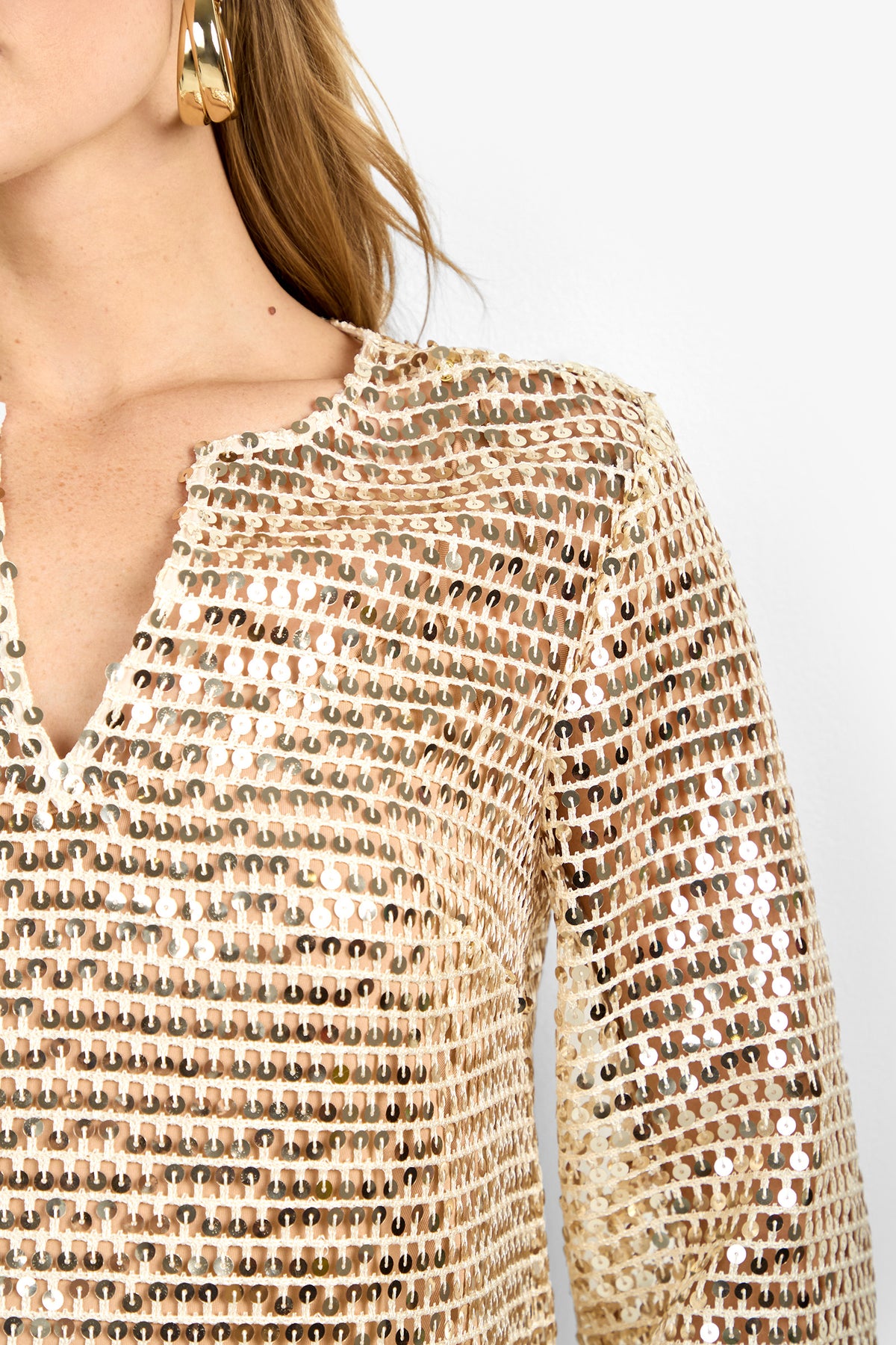 Close-up of a woman in the Mailani Top, featuring gold sequins, a notched neckline, and long sleeves. She wears large gold hoop earrings and has long hair against a plain white background.