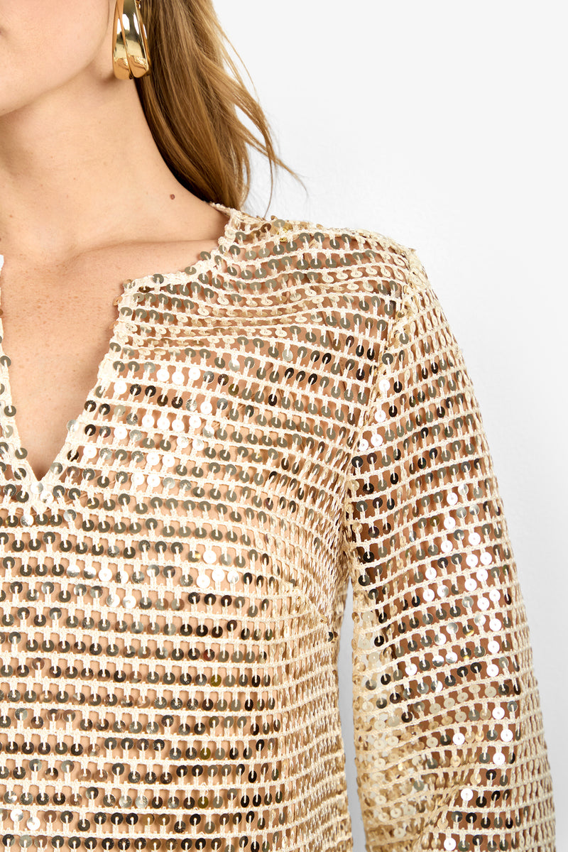 Close-up of a woman in the Mailani Top, featuring gold sequins, a notched neckline, and long sleeves. She wears large gold hoop earrings and has long hair against a plain white background.
