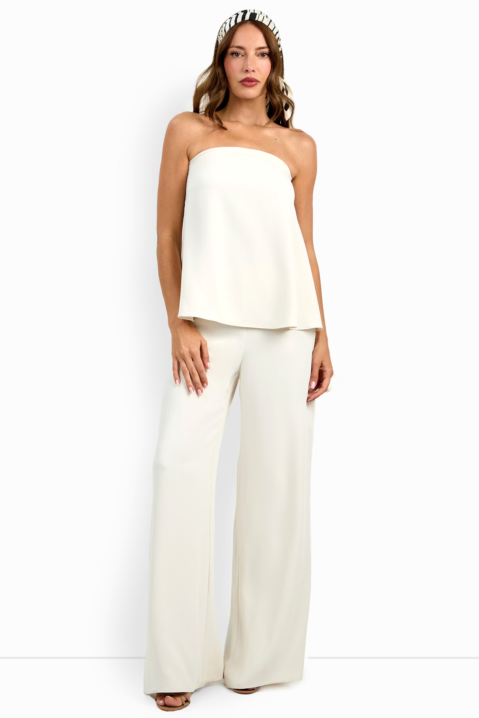 A woman wearing the strapless, flowy white Hulla Top with matching wide-leg pants and a black-and-white headband stands against a plain white background.