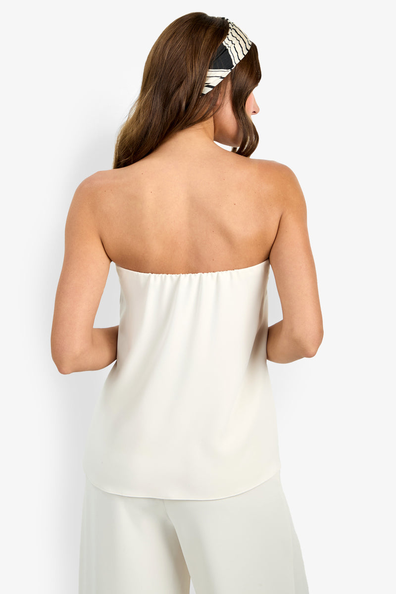 A woman with brown hair, seen from the back, models the Hulla Top—a white strapless top—paired with matching white pants and a black-and-white striped headband against a plain white background.