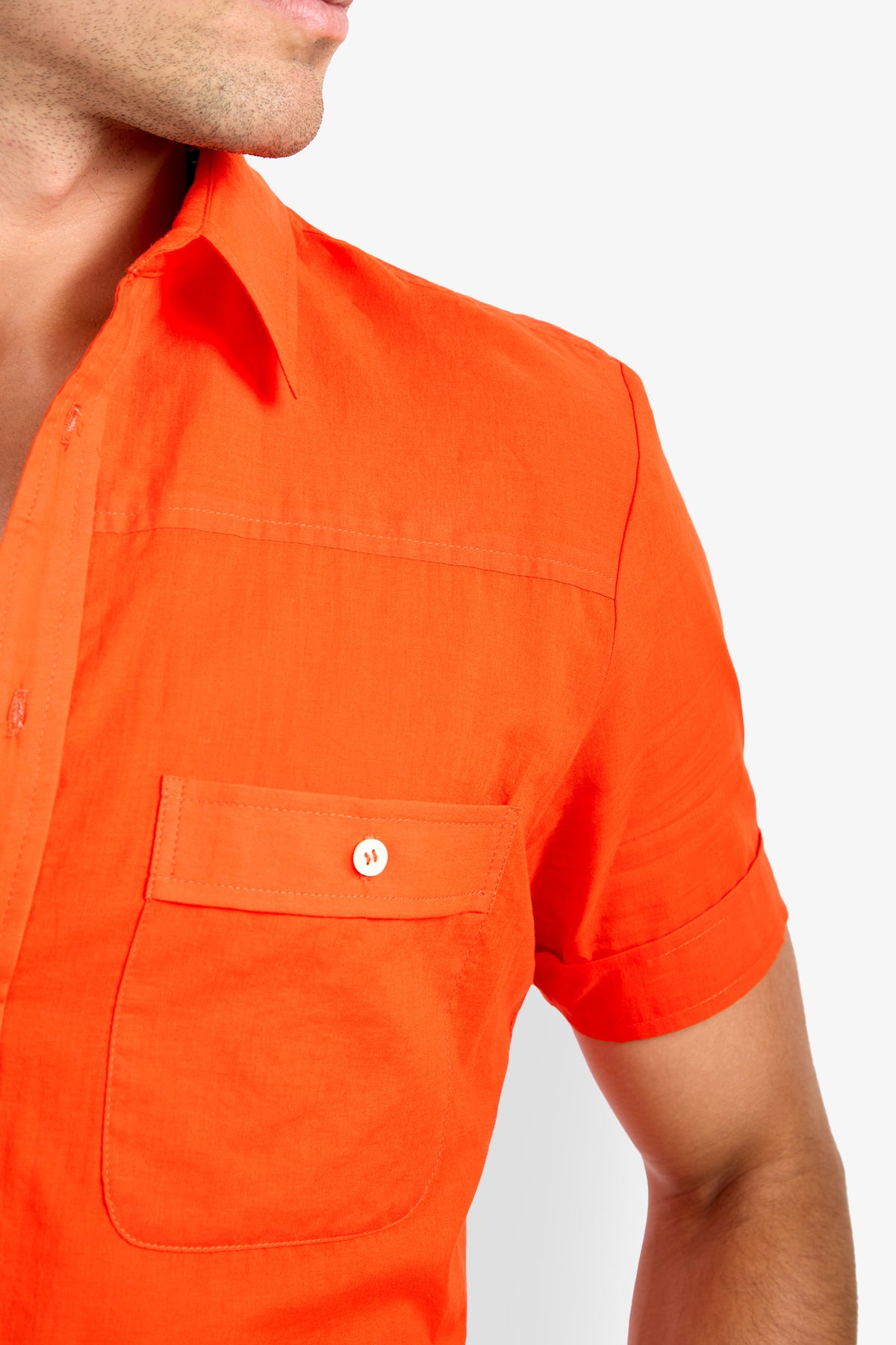 A person wearing the Will Shirt, a bright orange short-sleeve button-up with a front pocket, is shown from shoulders to mid-torso, facing slightly left against a white background.