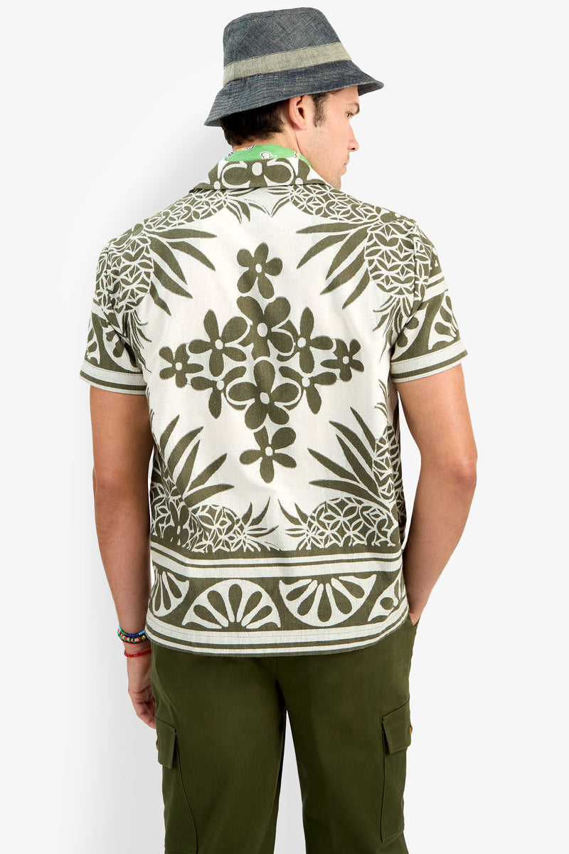 A person seen from behind wears a gray bucket hat, olive green cargo pants, and the Felix Shirt, which features a short-sleeve design with an olive green and white floral pattern.