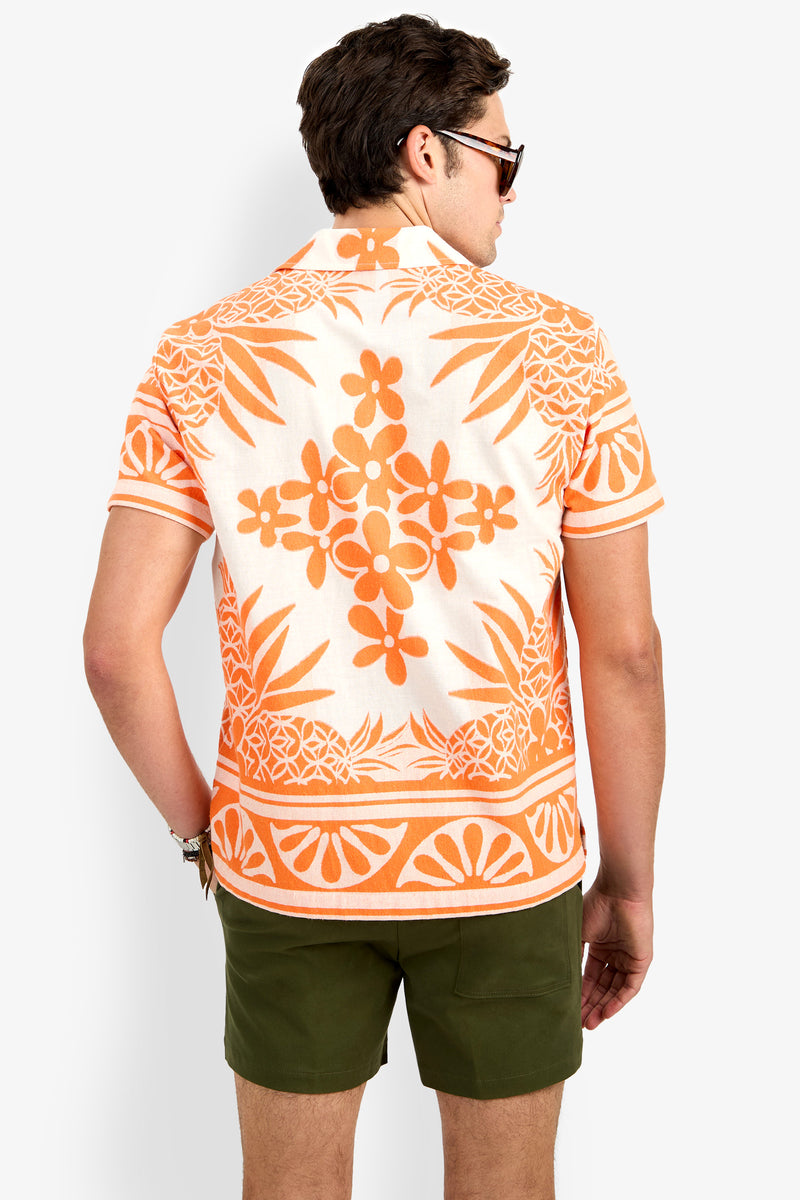 A man wearing the Felix Shirt, which features an orange and white floral pattern and short sleeves, paired with olive green shorts and sunglasses, is shown from the back against a plain light background.