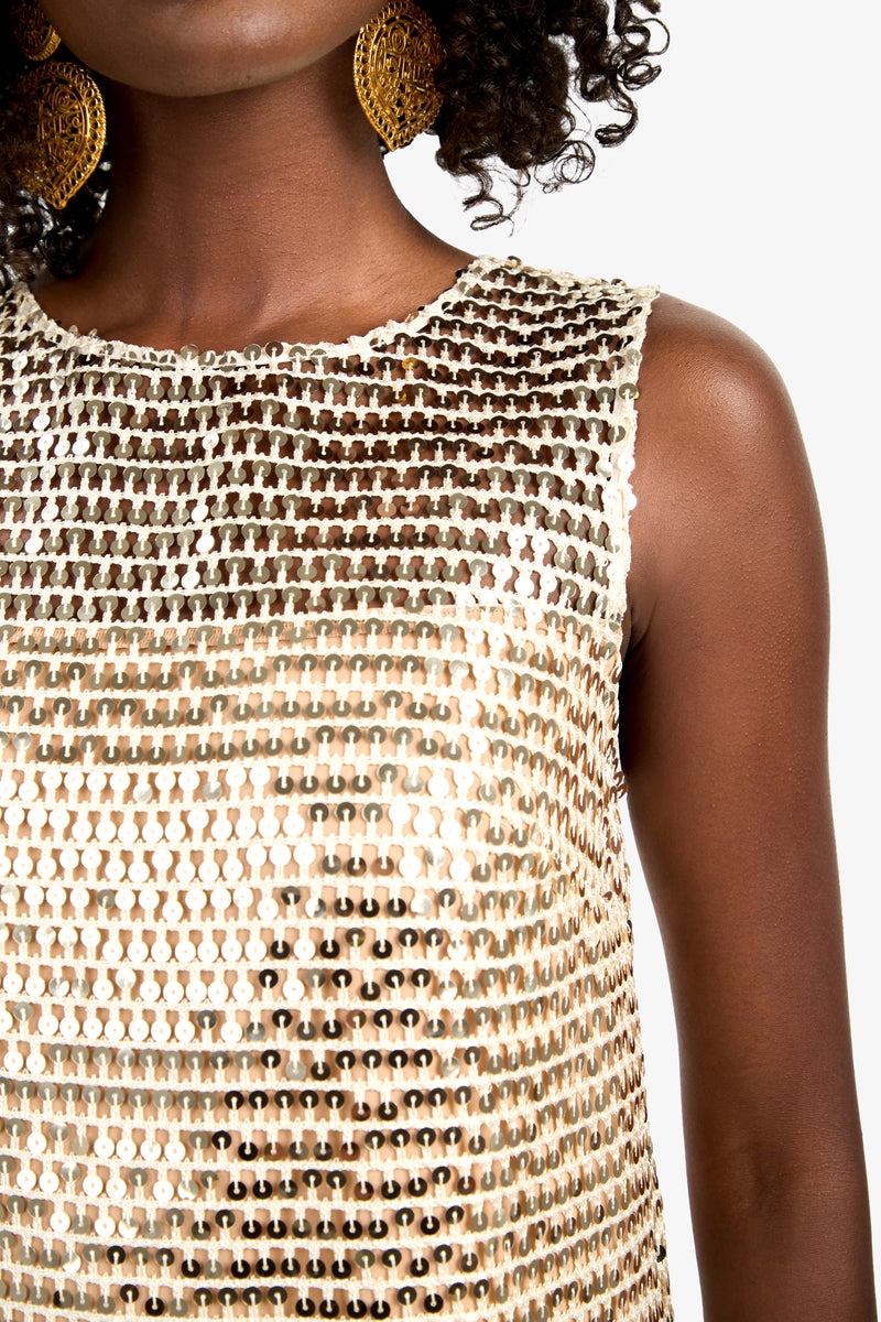 A woman models the Eleanor Dress, a sleeveless, gold sequin-covered design. Large gold earrings accent her look. Only her lower face and upper torso are shown against a white background.
