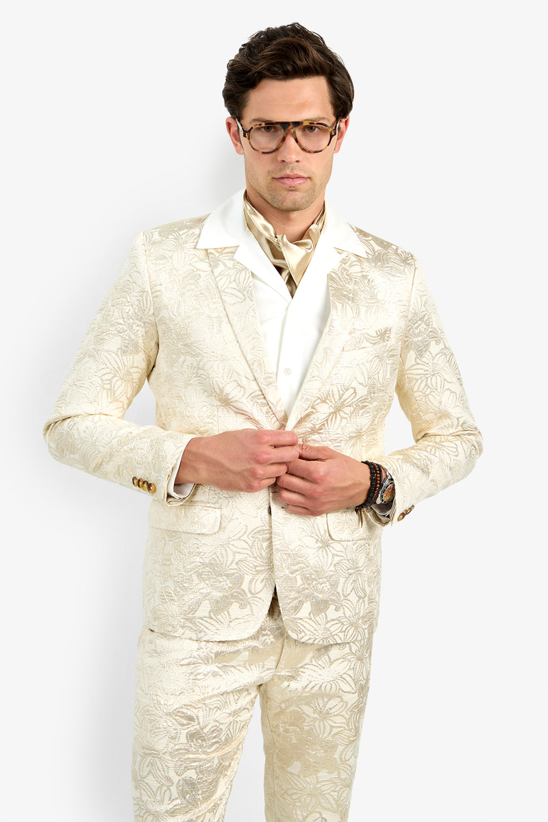 A man wearing glasses poses in the Thurston Blazer, a cream-colored floral-patterned suit jacket with a white shirt and patterned scarf, standing against a plain white background.
