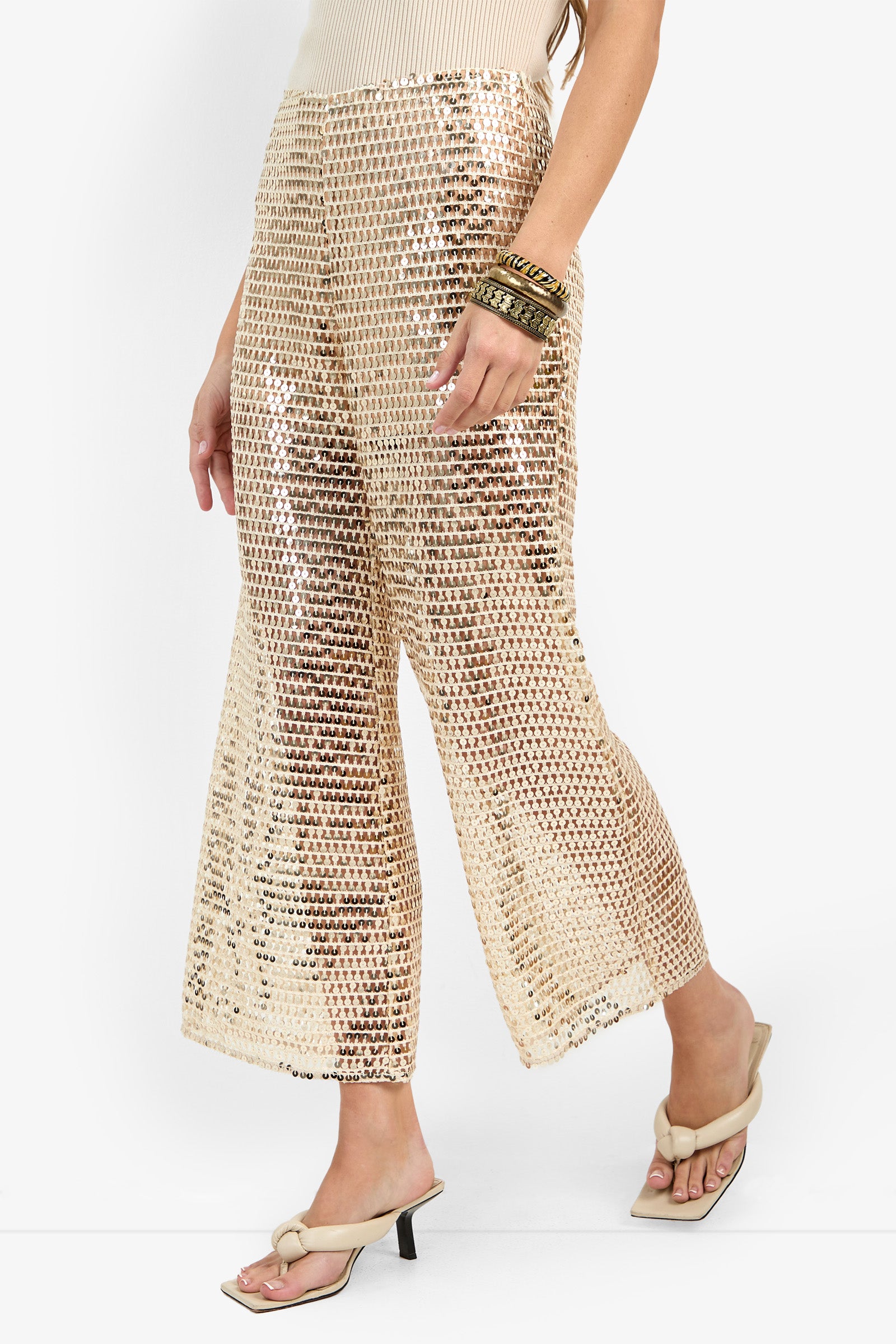 A person wearing the Dariya Pant—high-waisted, wide-leg gold sequin pants—with beige heeled sandals, stacked bangles, and a sleeveless top against a plain white background.