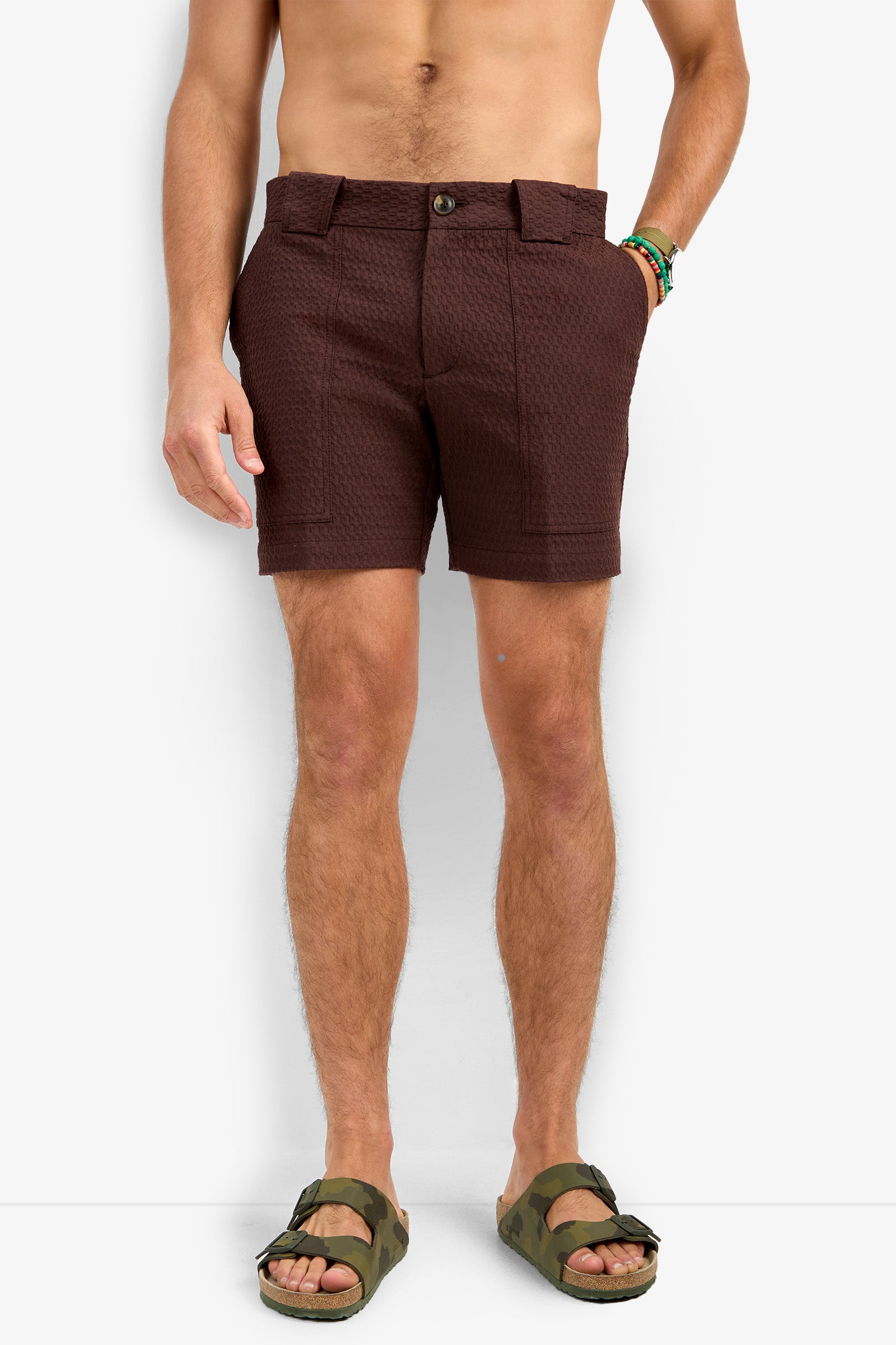 A shirtless person wears Randy Short textured brown shorts with front patch pockets, green camo sandals, and two beaded bracelets, standing against a plain white background.