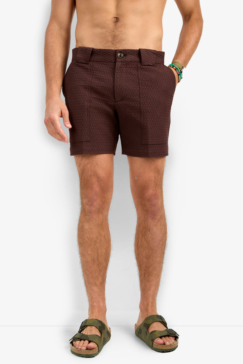 A shirtless person wears Randy Short textured brown shorts with front patch pockets, green camo sandals, and two beaded bracelets, standing against a plain white background.
