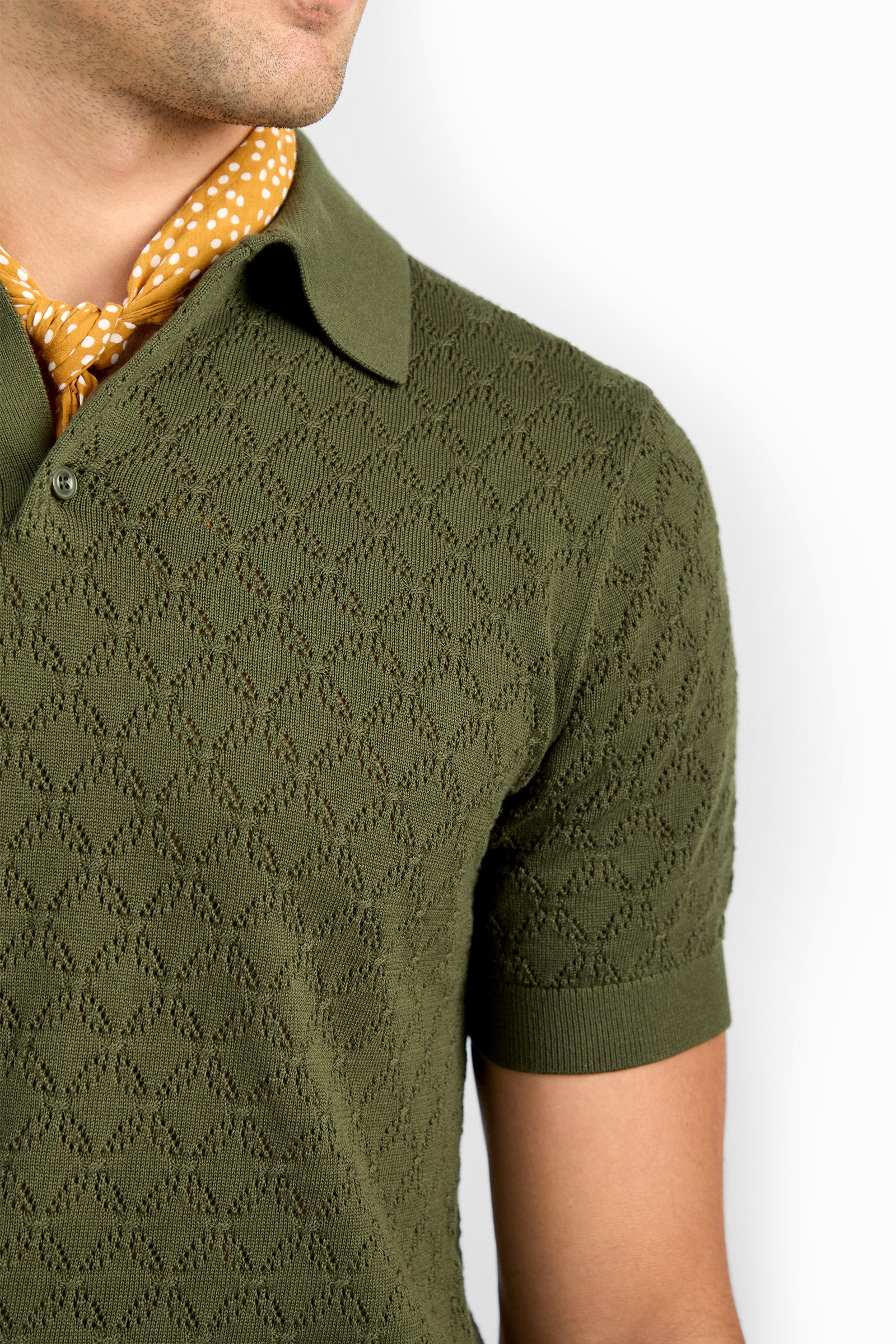 A person wearing the Waylen Short Sleeve Polo in olive green with a textured finish and collar, paired with a yellow polka-dot scarf around their neck, shown from the shoulders up against a white background.