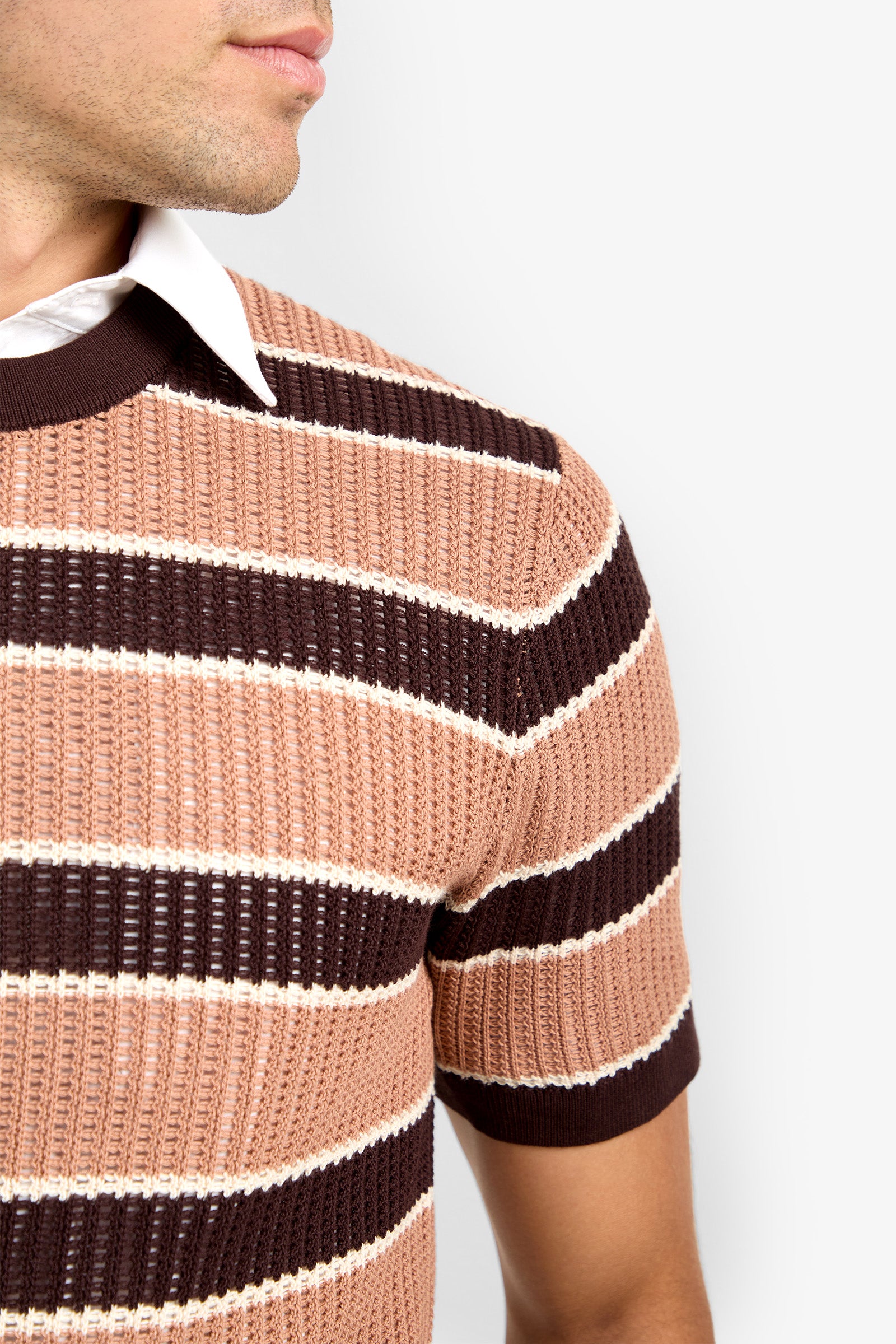 A man wears the Carlos Short Sleeve Crewneck, a brown, beige, and white striped knit shirt over a white collared shirt, shown from the nose down in profile against a plain light background.