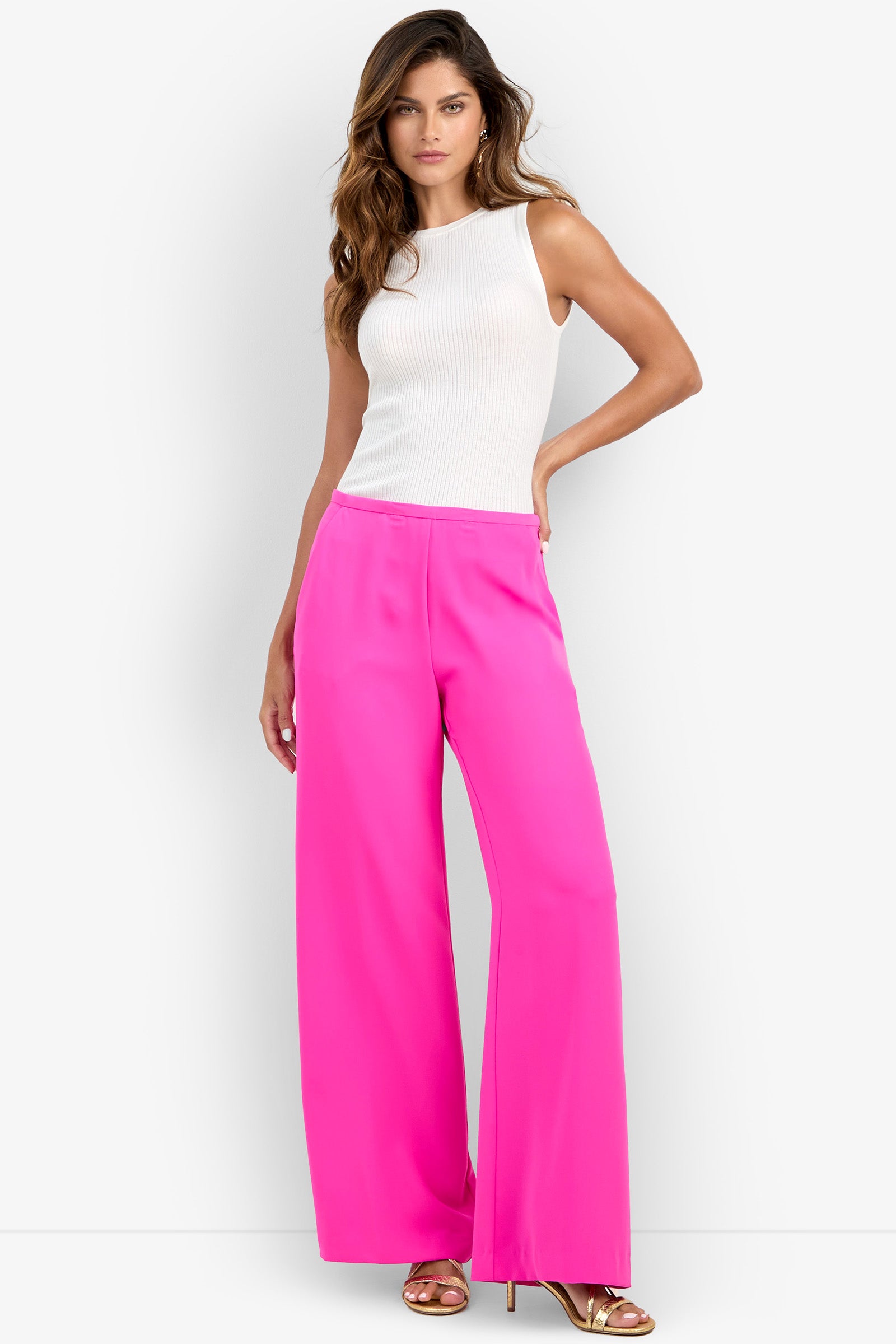 Model wearing the Lyndi Top in Luminosa Rosa, paired with bright pink wide-leg pants and gold heels, posing with one hand on her hip against a plain white background.