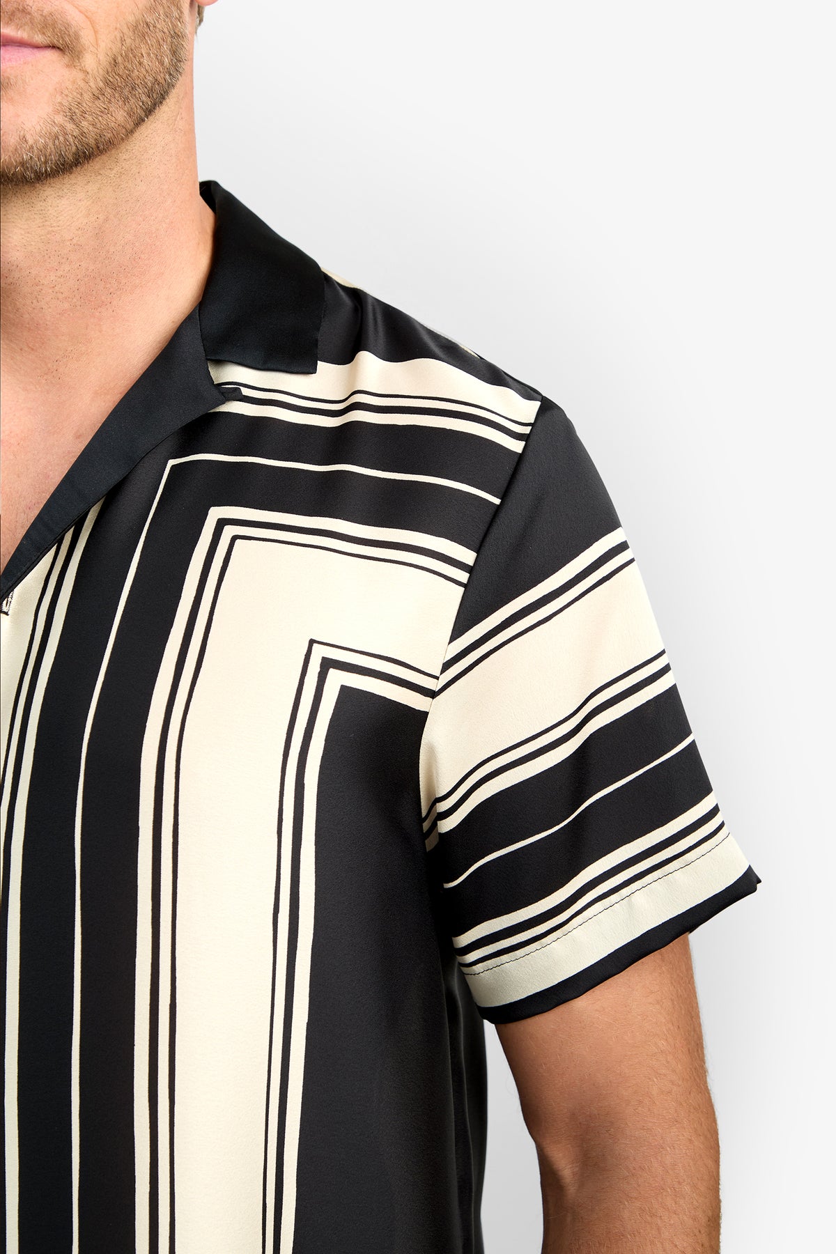 A close-up of a person wearing the Felix Camp Shirt, a short-sleeve, black and cream striped collared shirt, photographed from the shoulder up against a plain background.