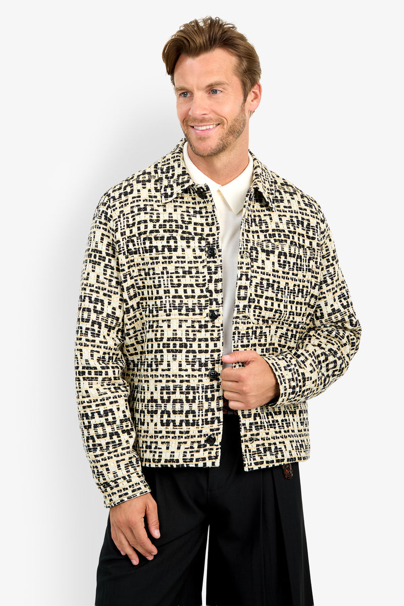 A man stands against a plain white background, smiling and holding his open PIERRE JACKET—featuring a cream and black pattern—over a white shirt.