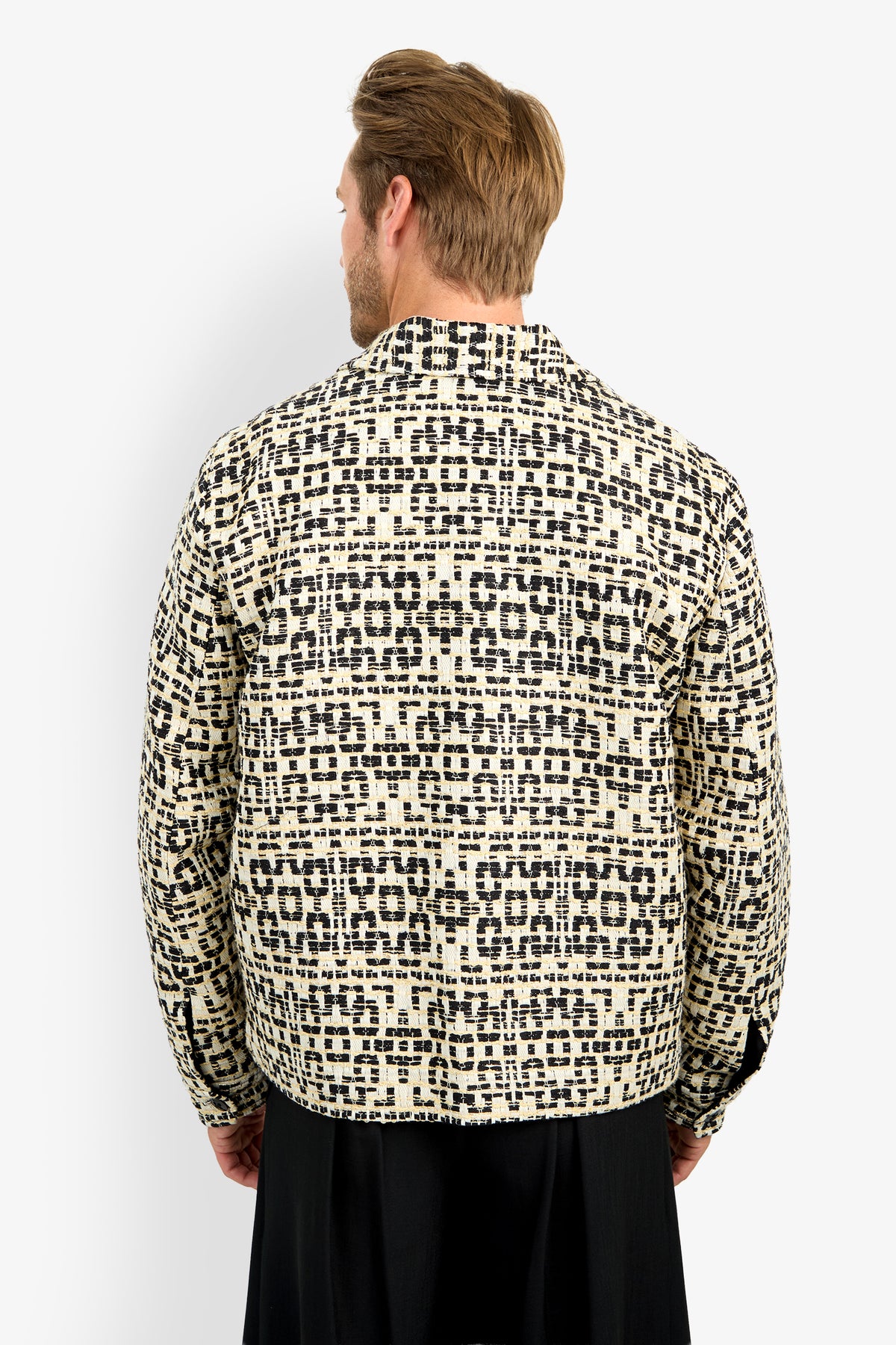 A man with light brown hair is seen from behind, wearing the PIERRE JACKET featuring a cream and black geometric pattern, standing against a plain white background.