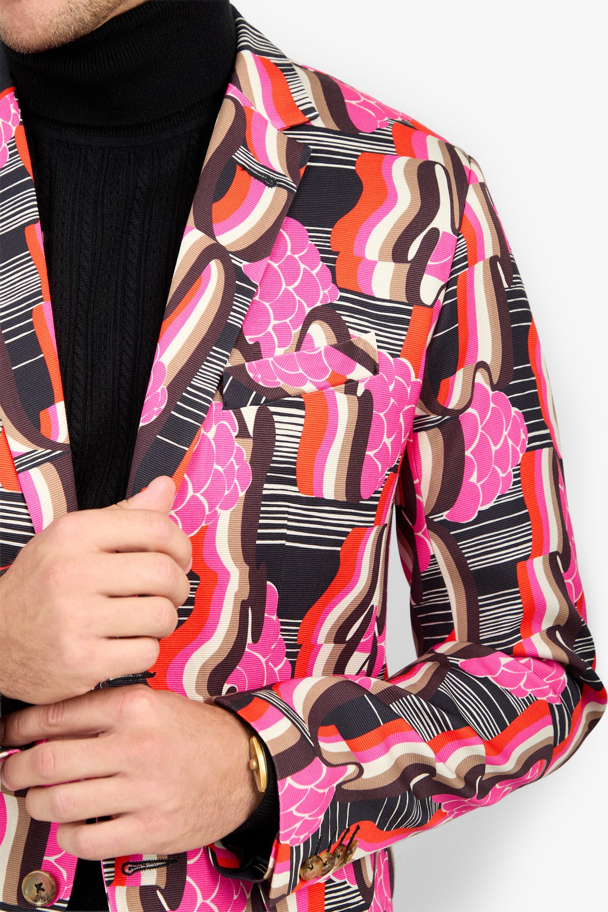 A person wears the THURSTON BLAZER—pink, red, brown, and black abstract pattern—over a black turtleneck. Only the torso and left hand are visible.