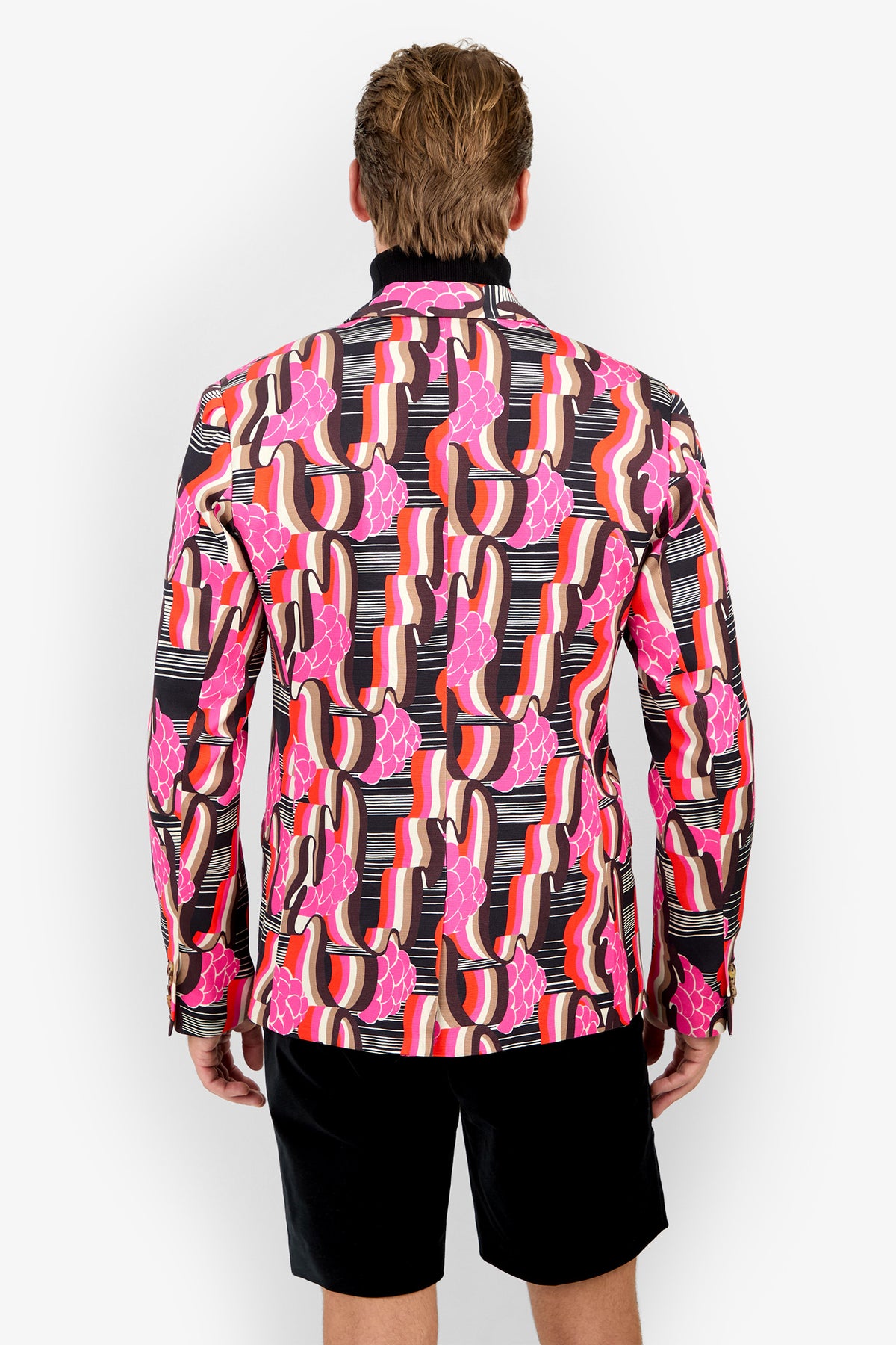 A person stands facing away, wearing the THURSTON BLAZER with bold pink, red, and black abstract patterns, paired with black shorts against a plain white background.