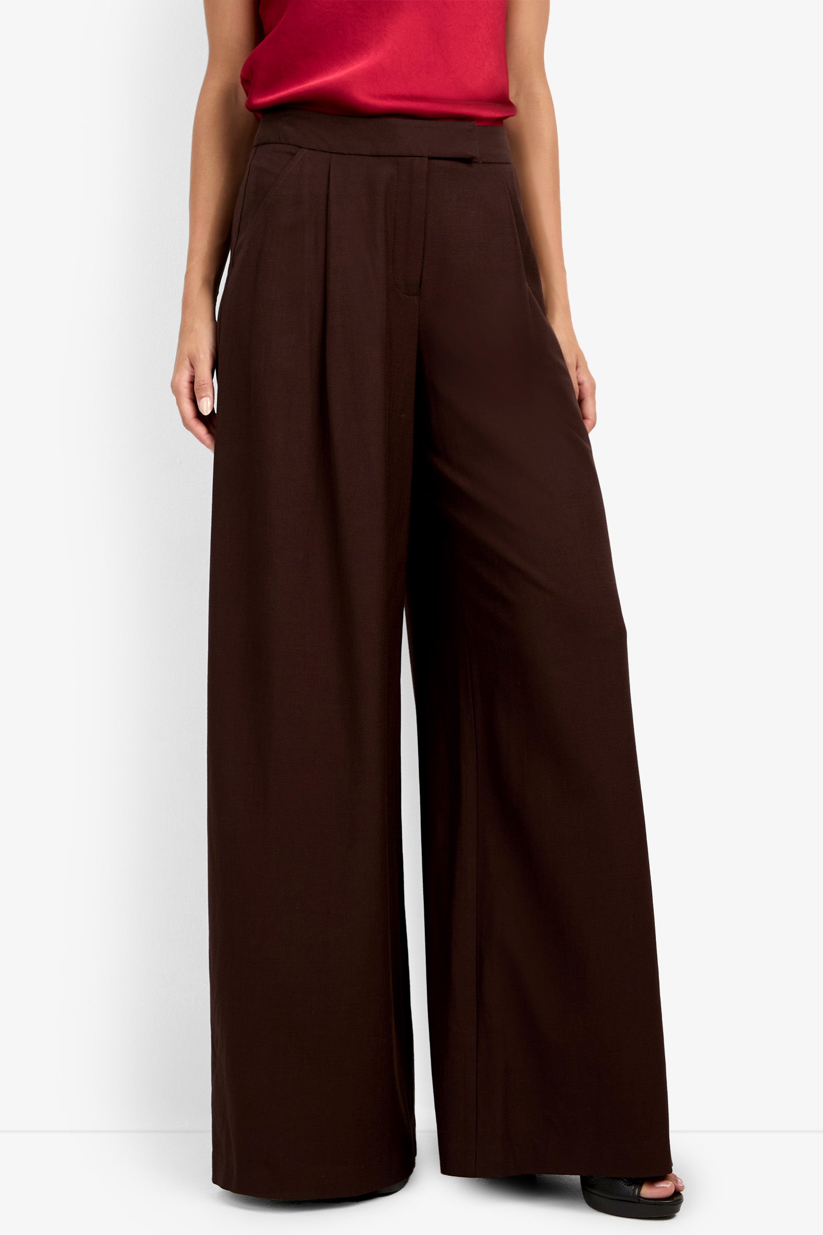 The lower half of a person wearing the MIMMO PANT, high-waisted wide-leg dark brown trousers, paired with a sleeveless red top, shown against a plain white background.