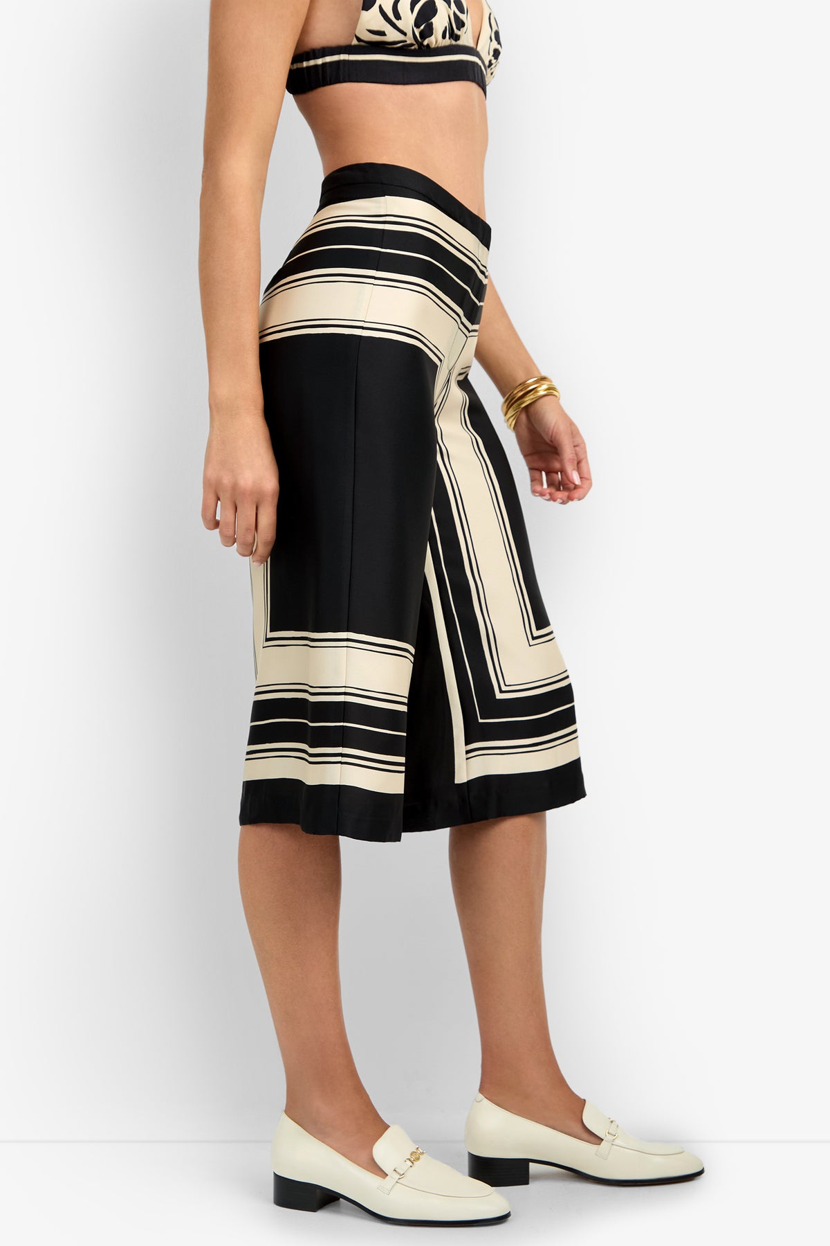 A person wearing the LANAY CROP PANT in black and beige geometric print with a matching crop top, white block-heeled loafers, and gold bangles stands against a white background.