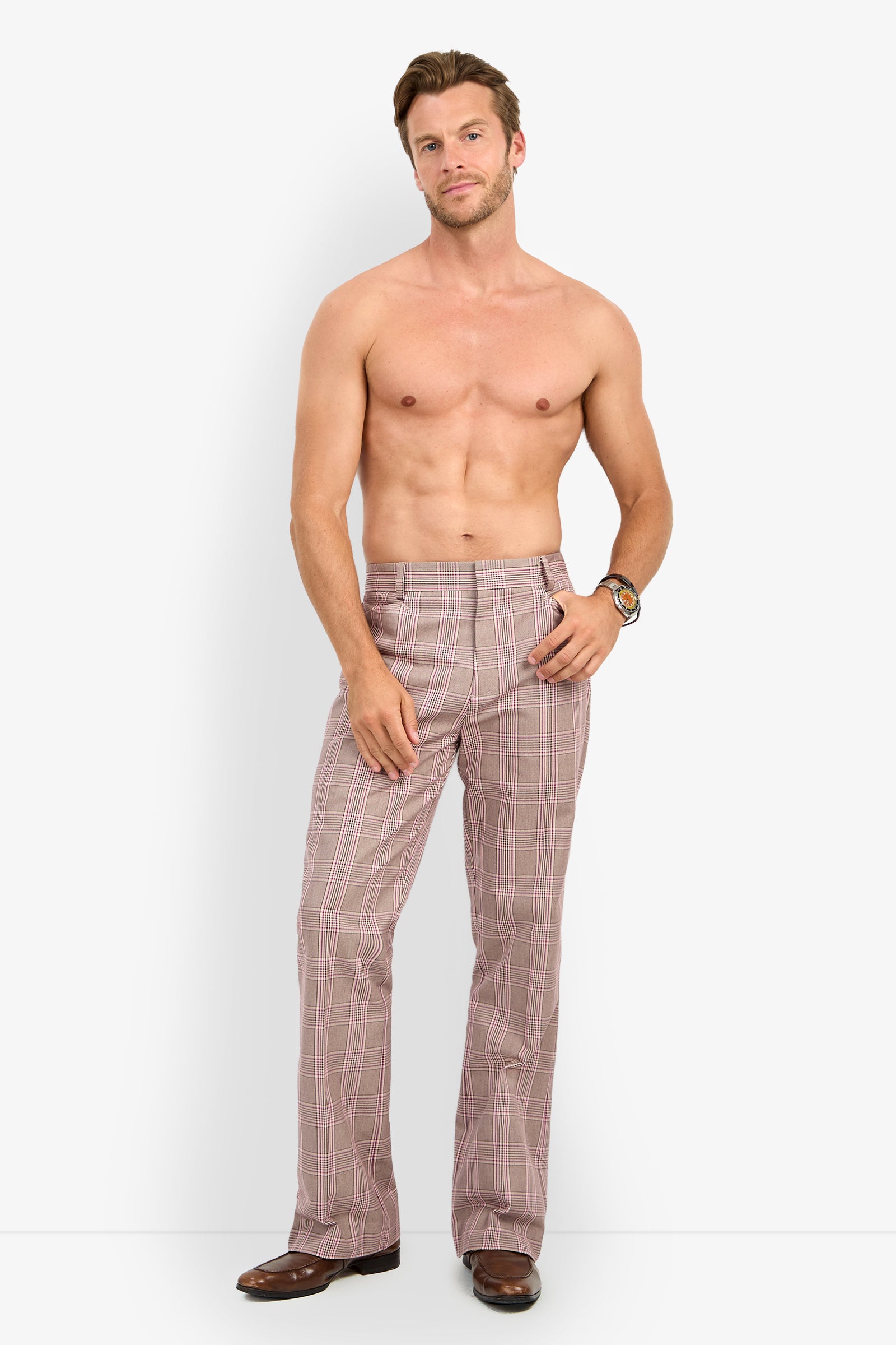A shirtless man wearing the Alejandro Bootleg Trouser, paired with brown dress shoes and a wristwatch, stands against a plain white background, gazing at the camera with a relaxed expression and one hand in his pocket.