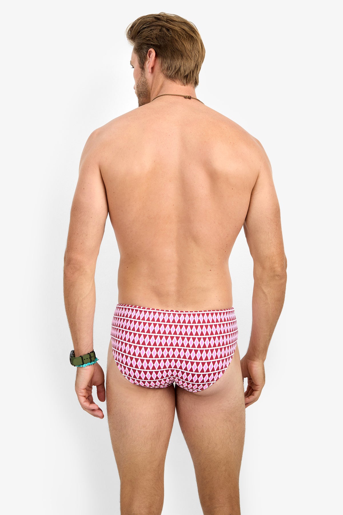 A man with short brown hair stands with his back to the camera, wearing the red and white BONDI SWIM BRIEF. He is shirtless, accessorized with a watch and bracelet, against a plain white background.