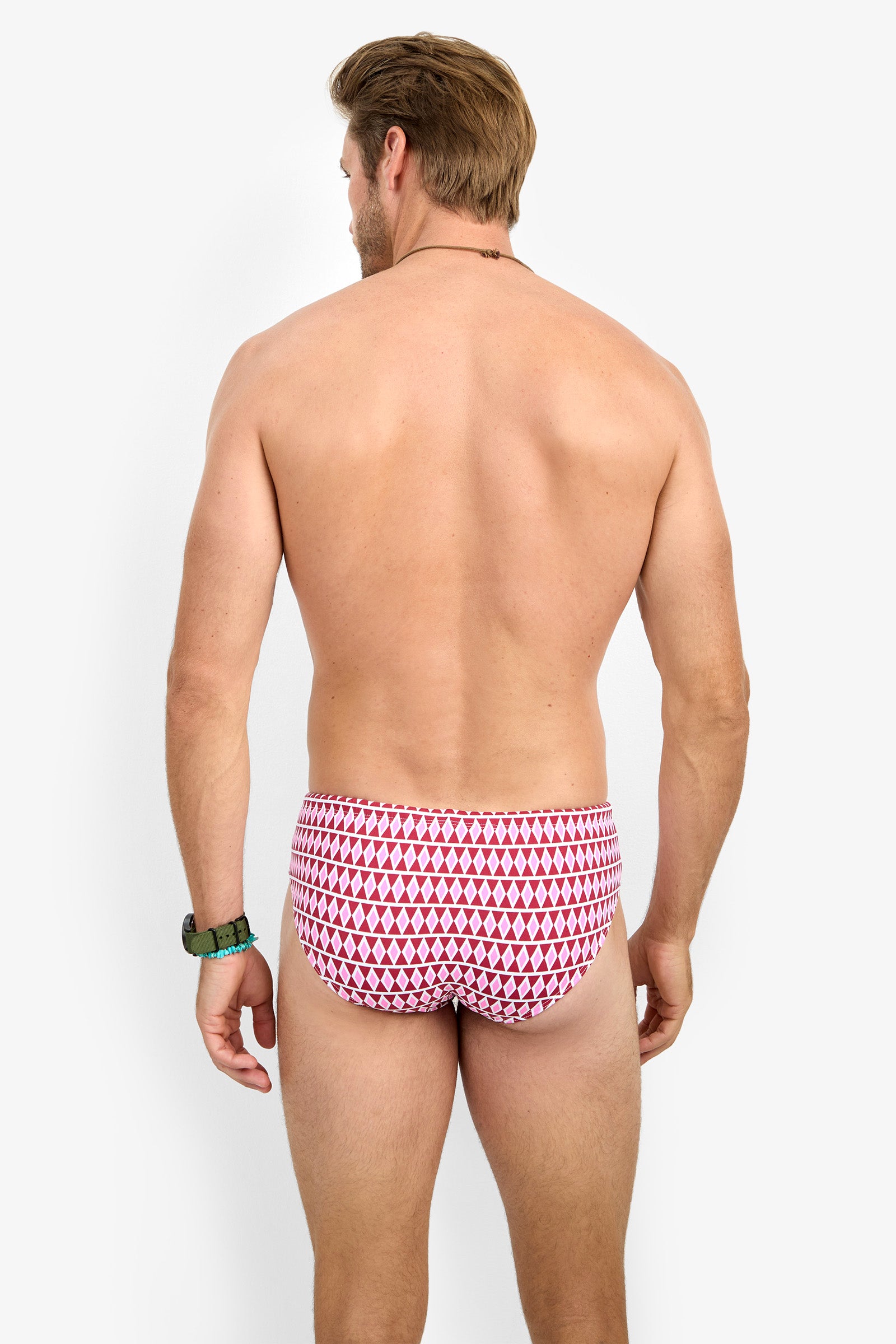 A man with short brown hair stands with his back to the camera, wearing the red and white BONDI SWIM BRIEF. He is shirtless, accessorized with a watch and bracelet, against a plain white background.
