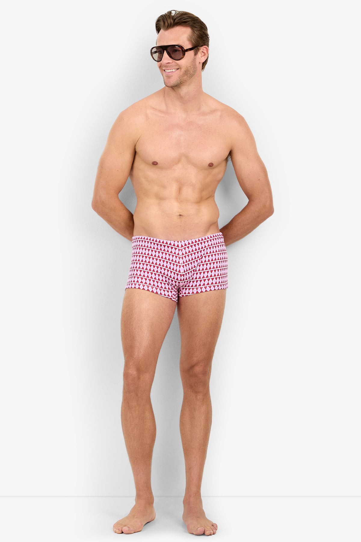 A smiling man in MONTEGO BAY SWIM TRUNK and sunglasses stands barefoot against a plain white background.